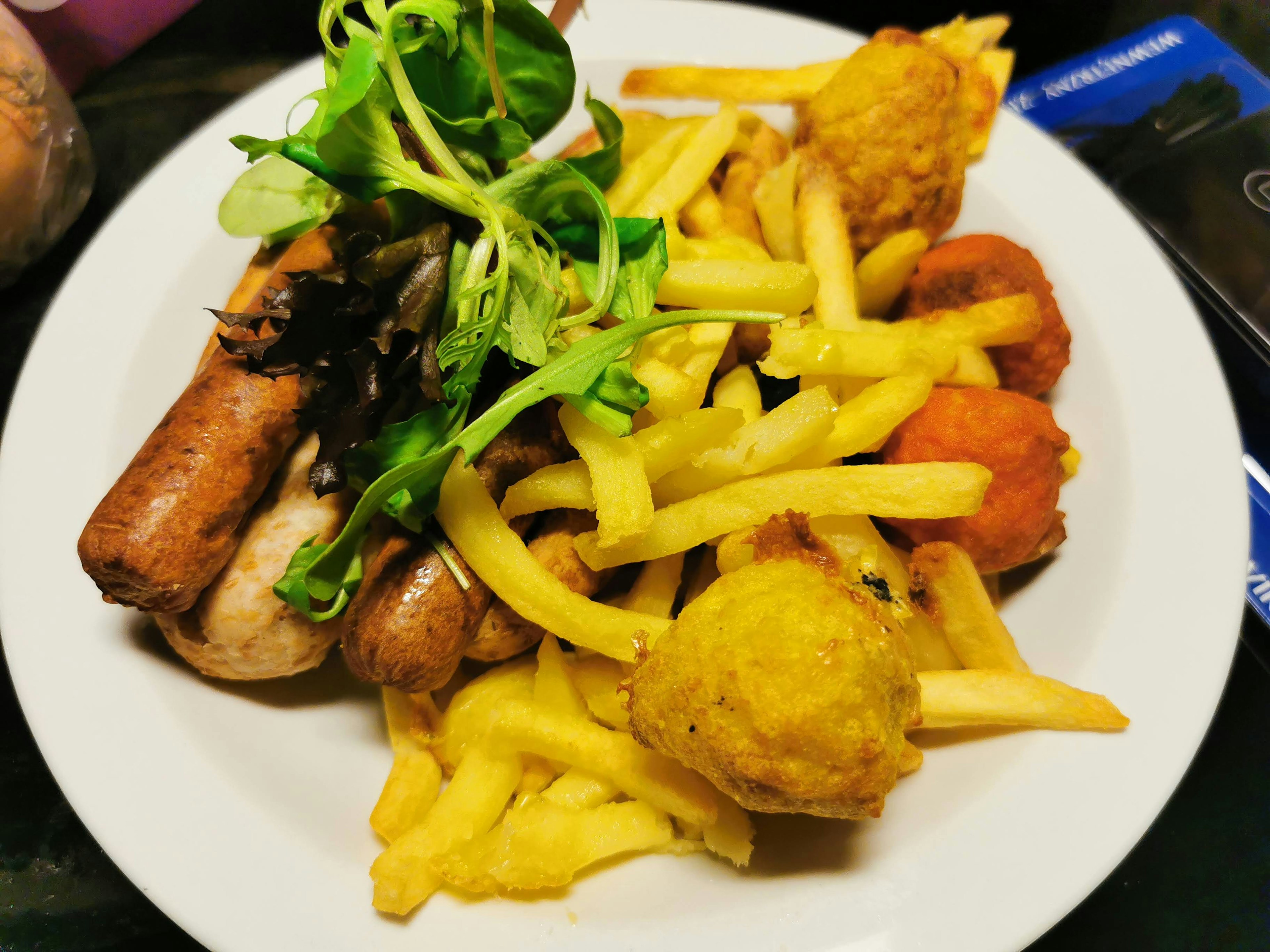 A plate featuring a mix of sausages, French fries, and garnished with fresh greens