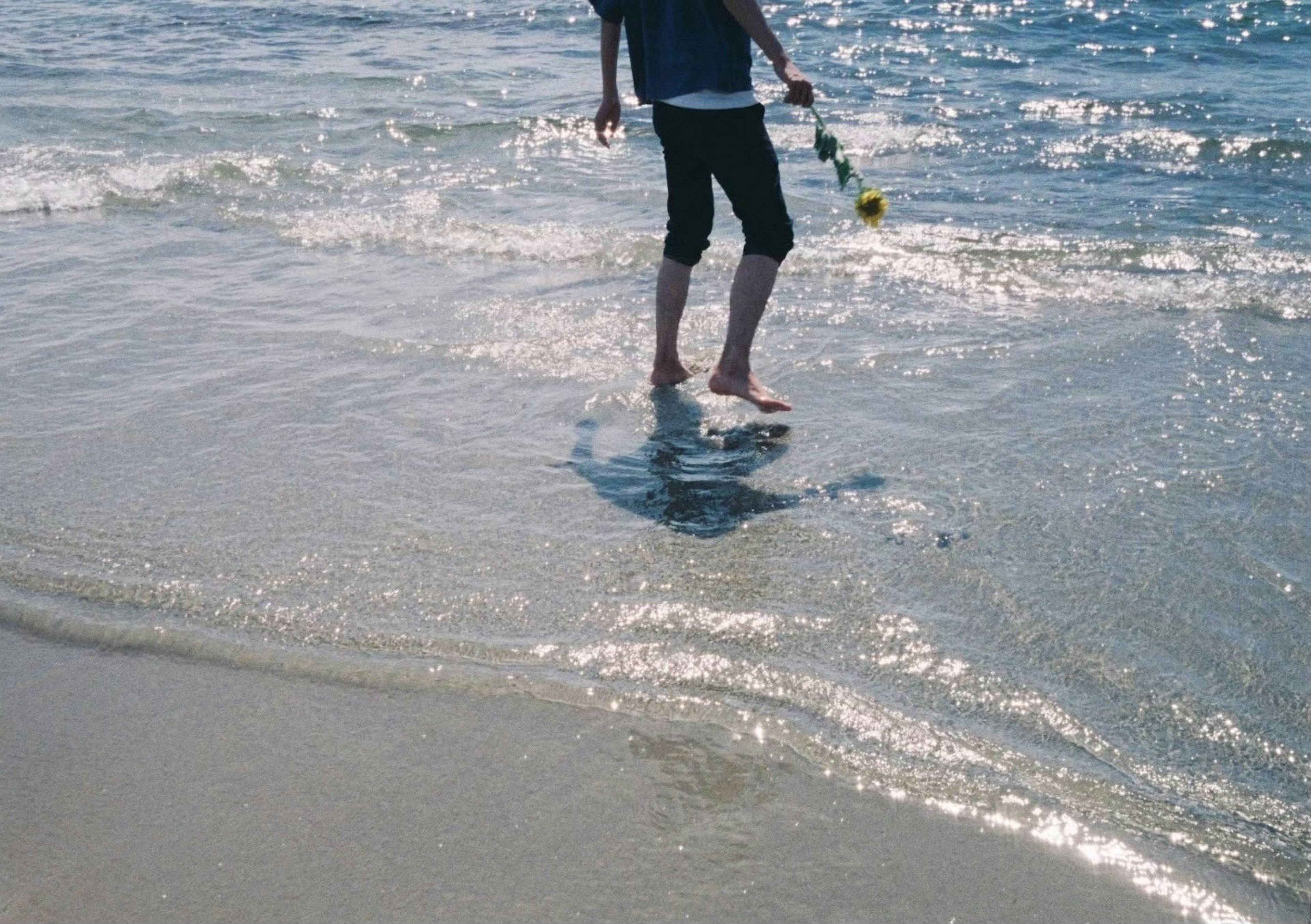 Person walking in shallow water on a beach with sunlight reflecting on the surface