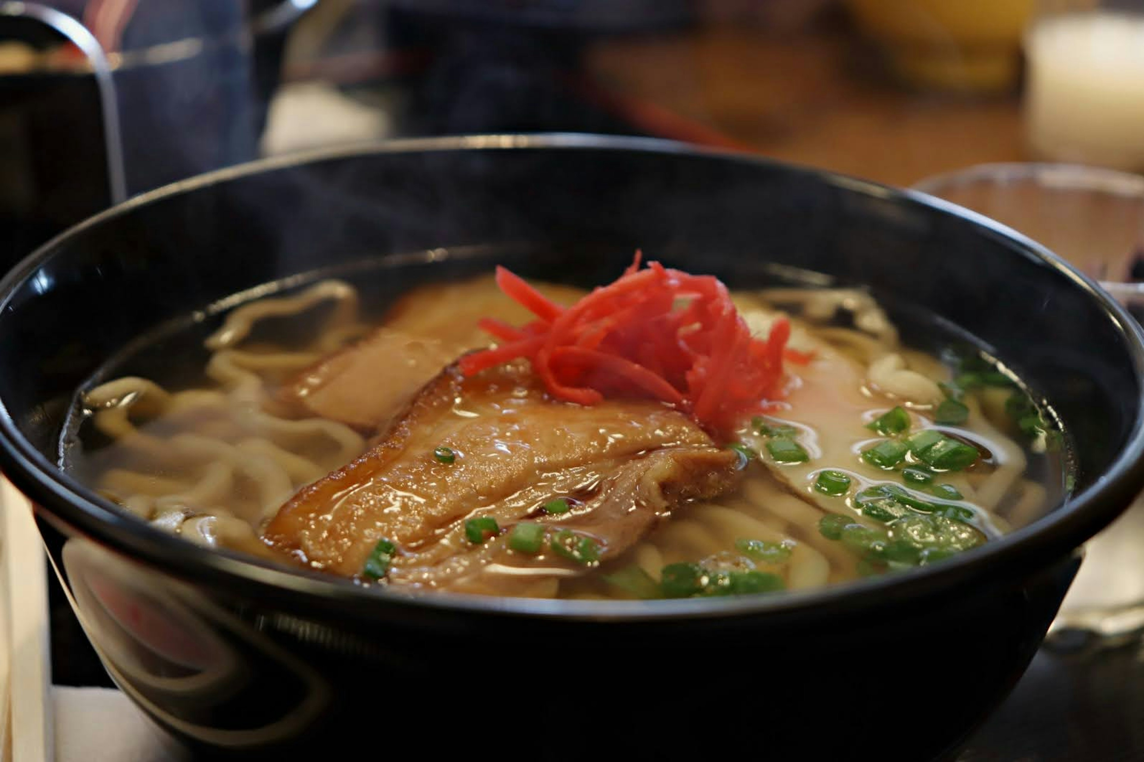 Tazón de ramen humeante con rodajas de chashu y jengibre encurtido