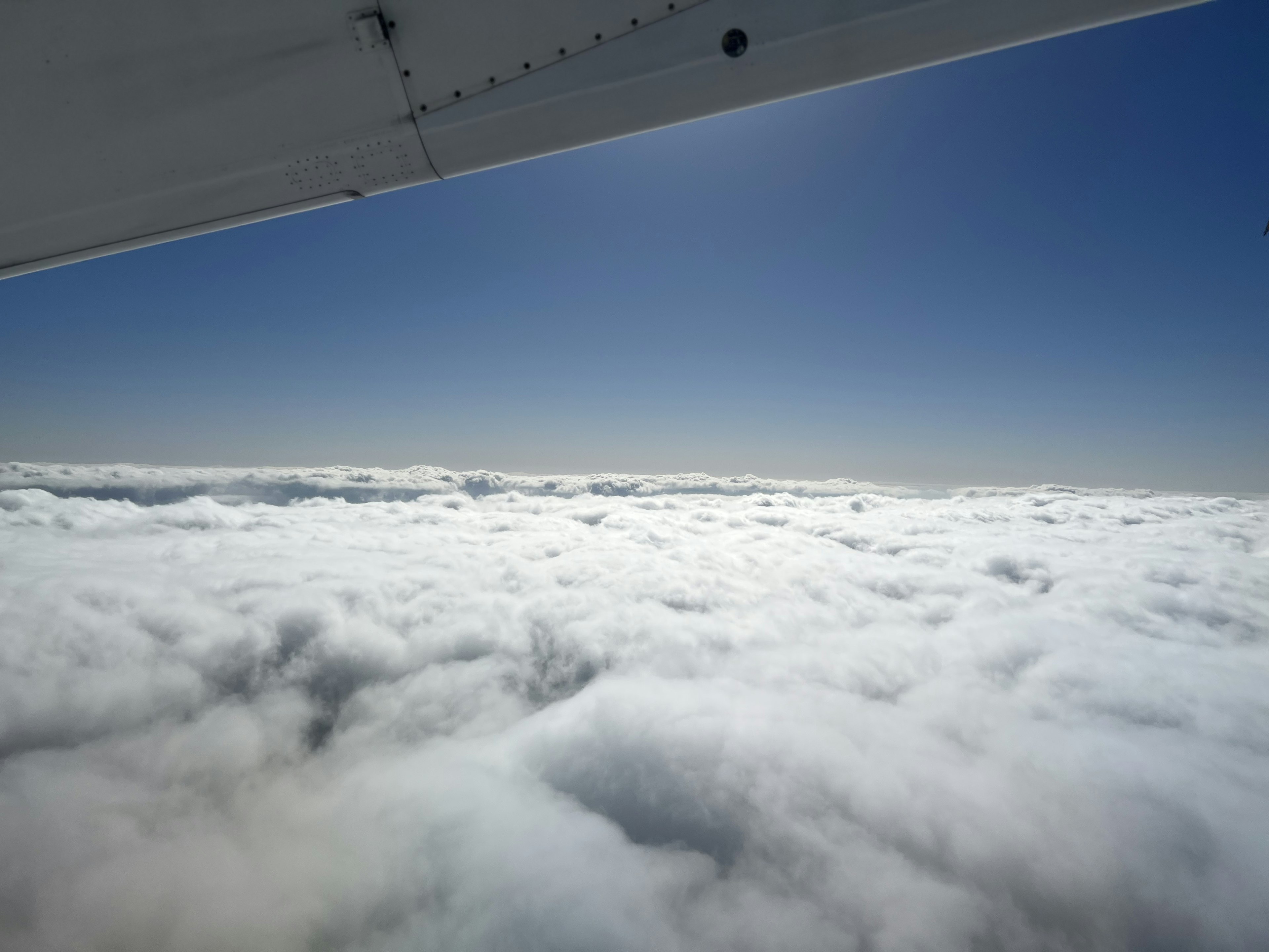 A vast sea of clouds under a blue sky with a partial view of an airplane wing