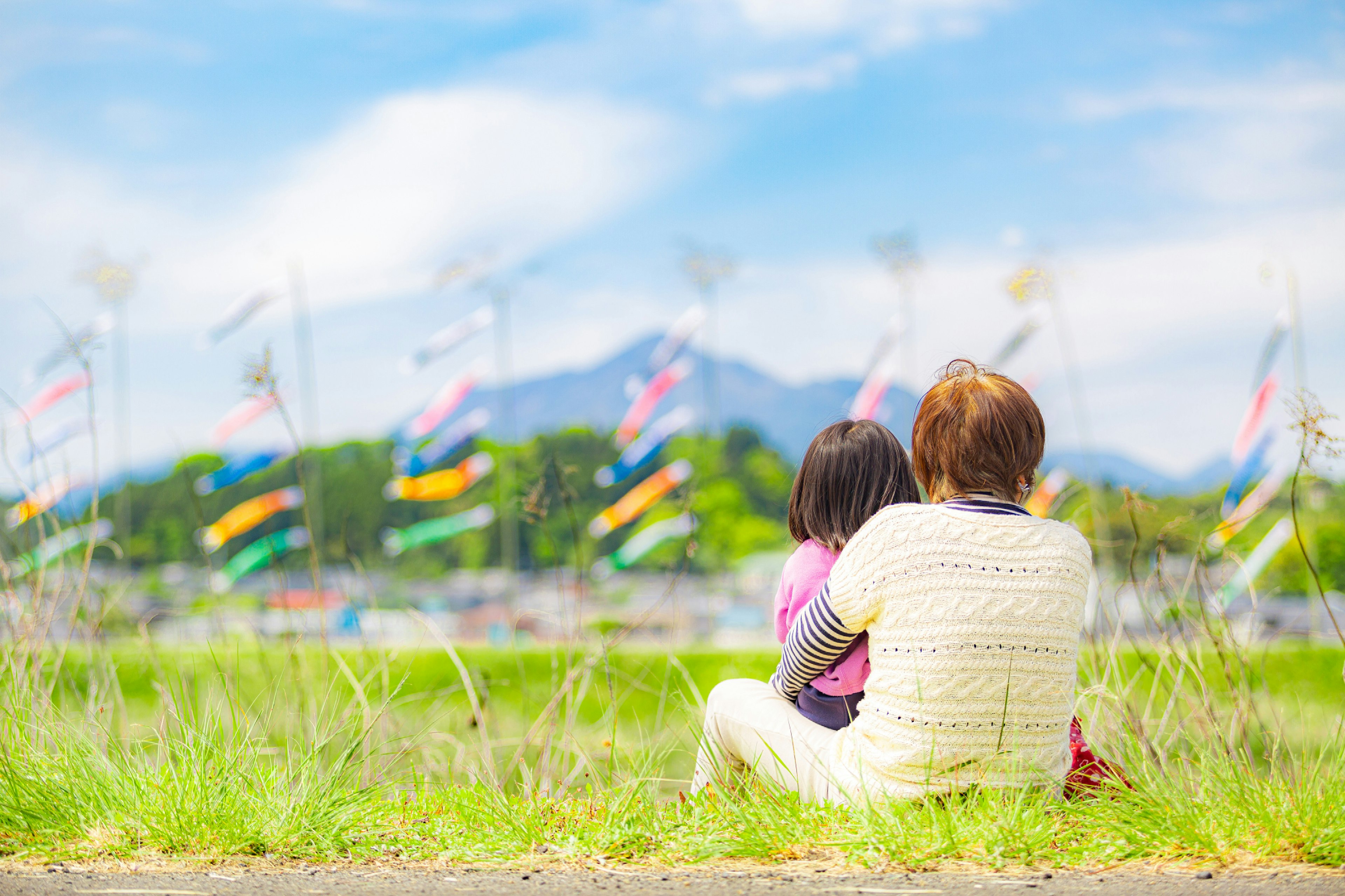 青空と風に揺れる鯉のぼりを背景に、子供を抱く母親の後ろ姿