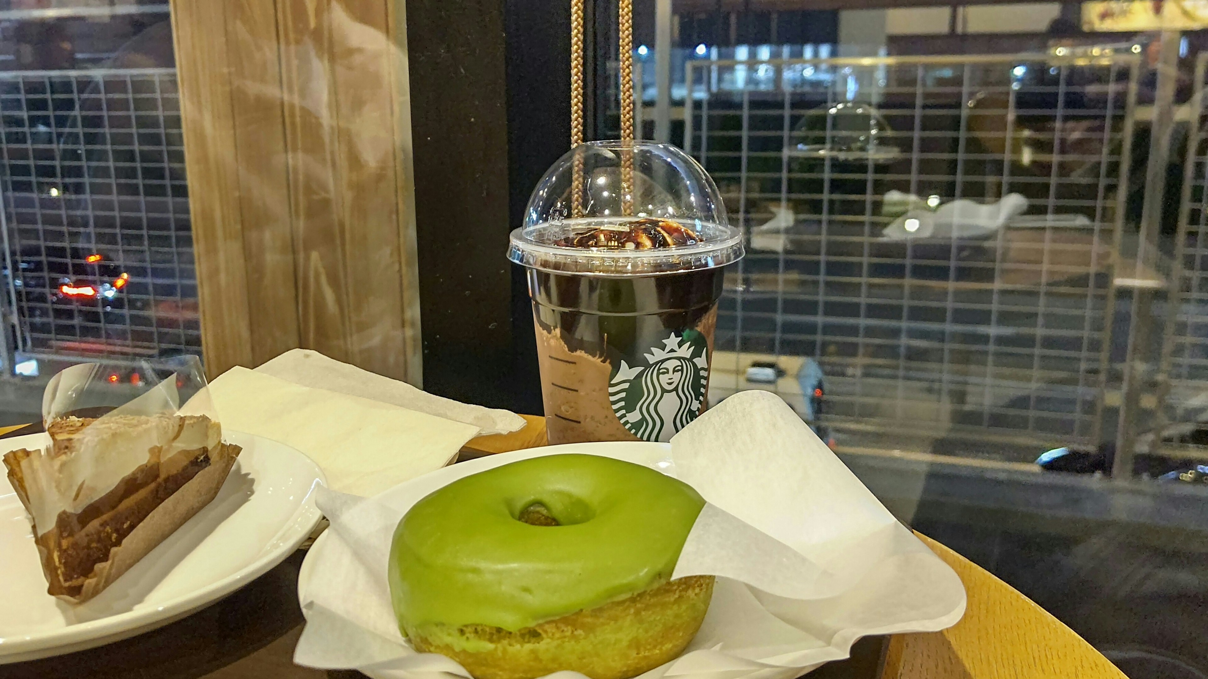 Green donut and coffee drink on a table with food plate and night view outside the window