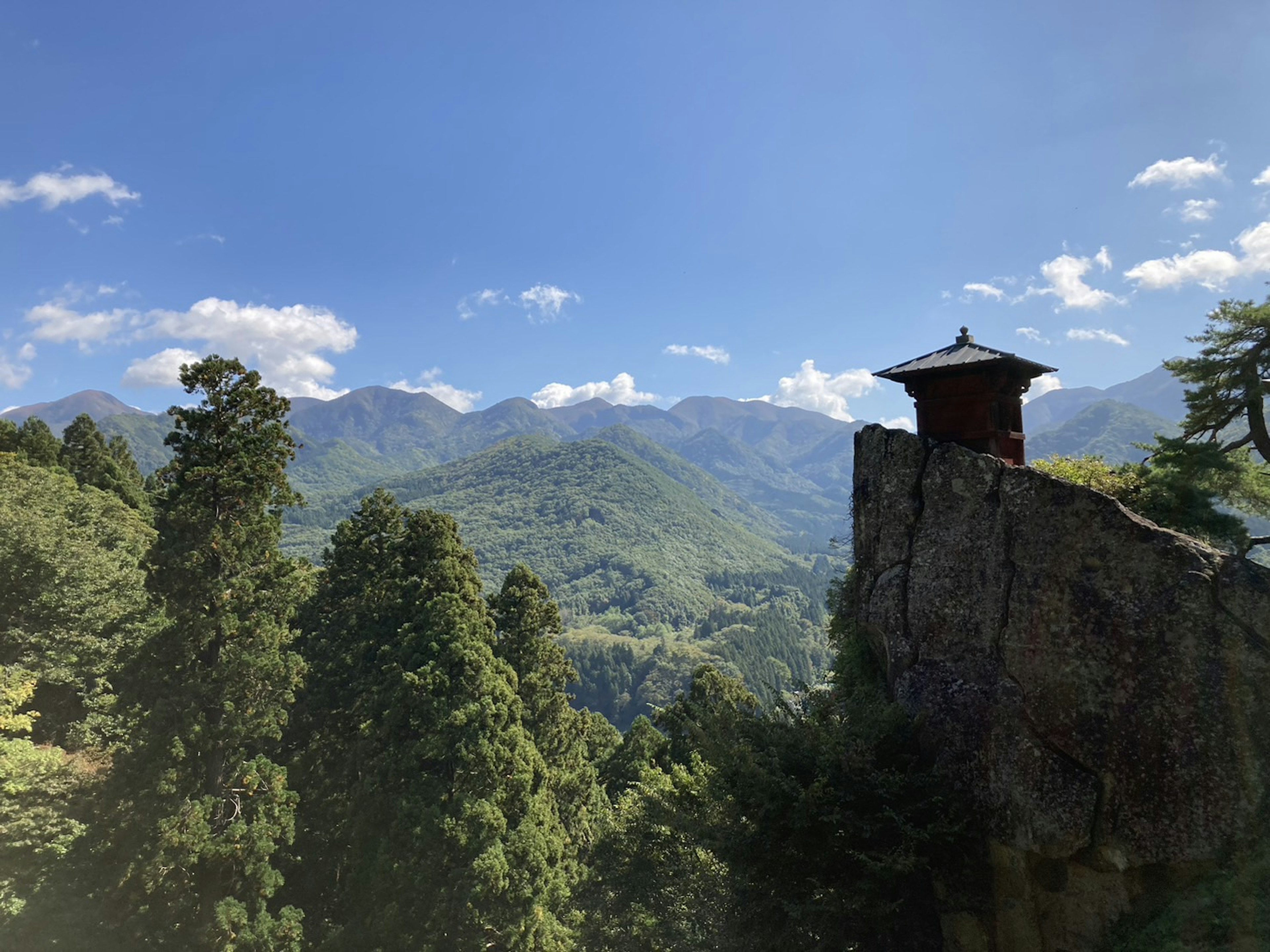 一座小屋坐落于岩石上，背景是山脉和树木