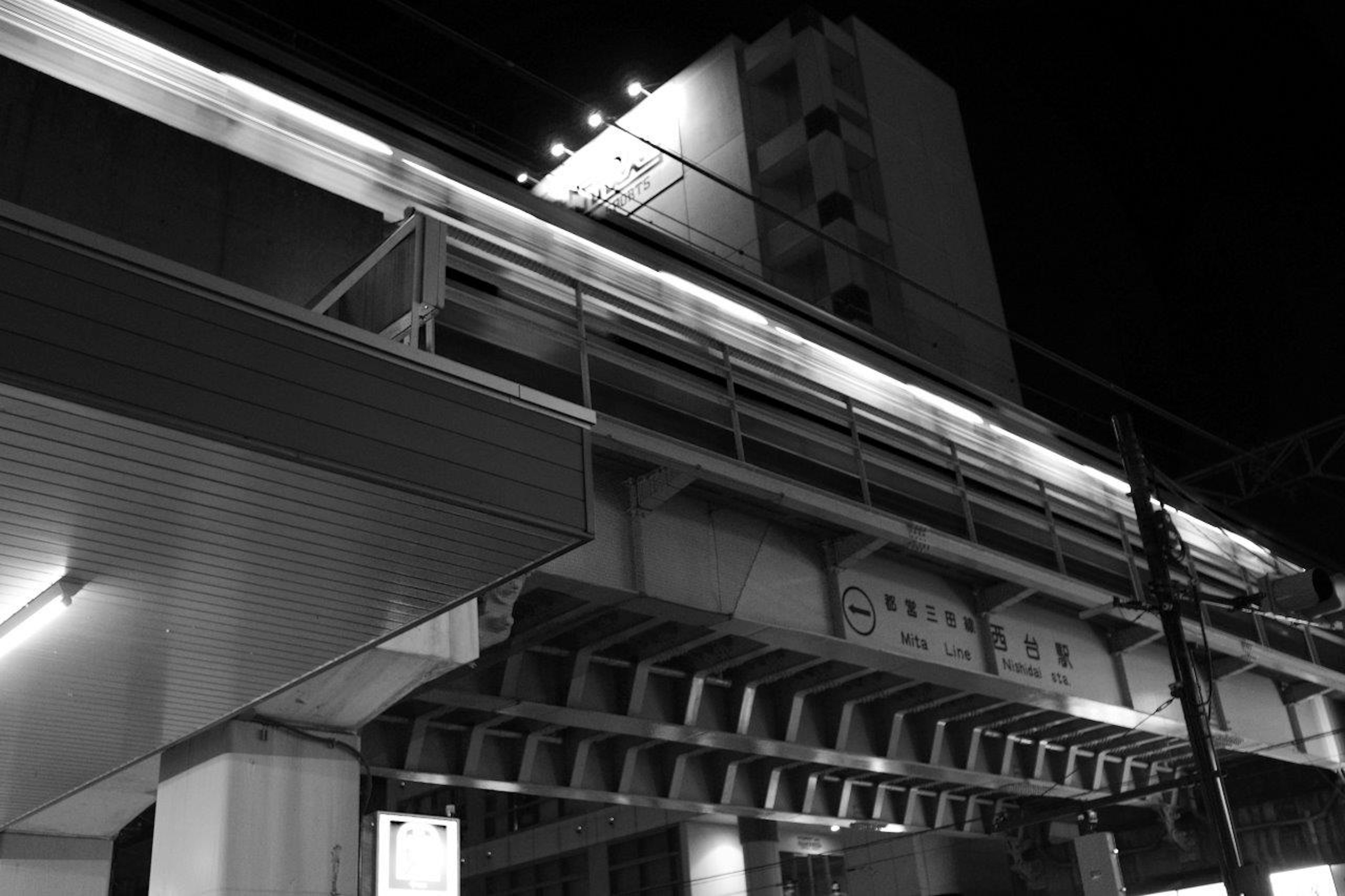 Foto en blanco y negro de un monorraíl elevado y un edificio por la noche