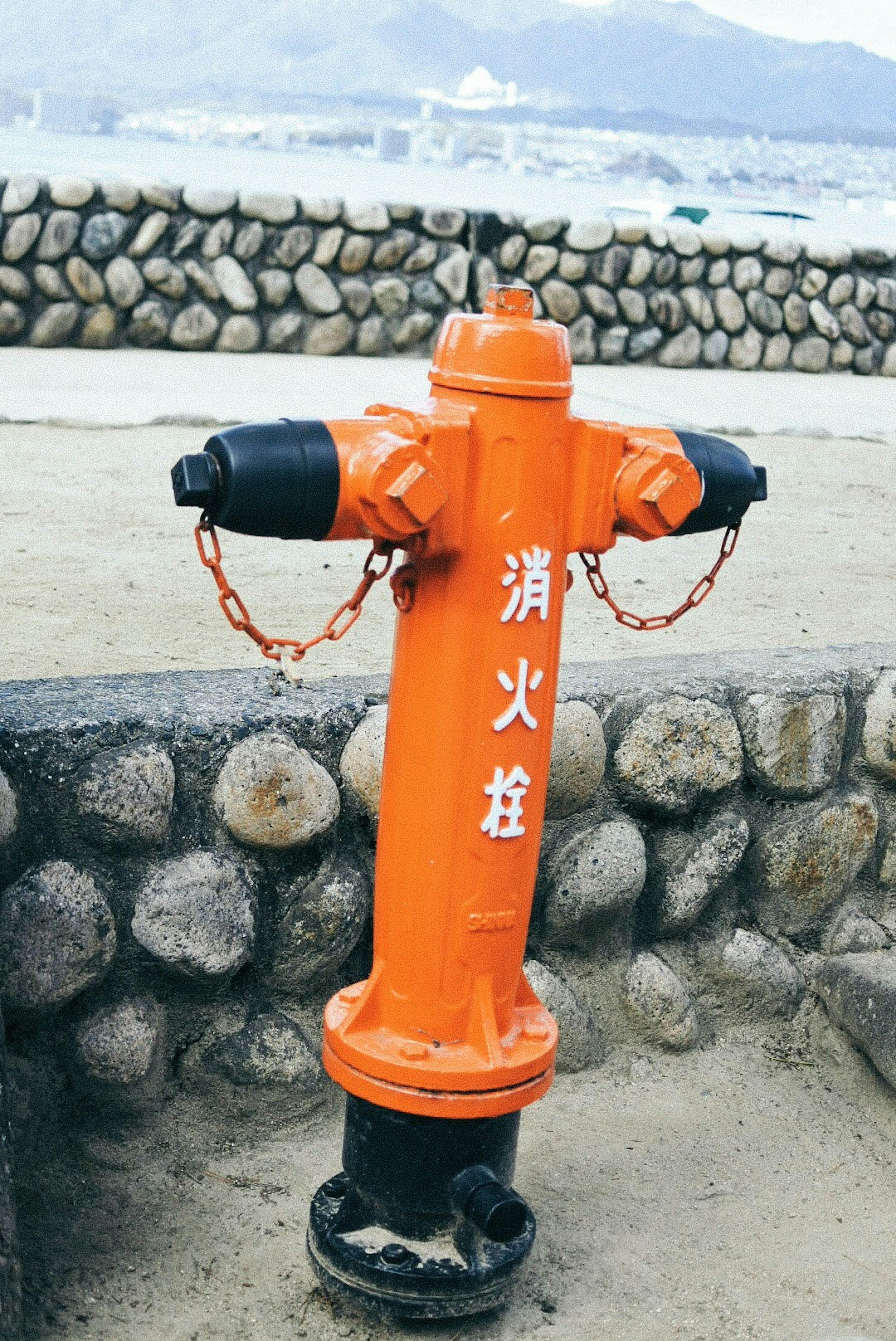 Sebuah hydrant oranye berdiri di depan dinding batu