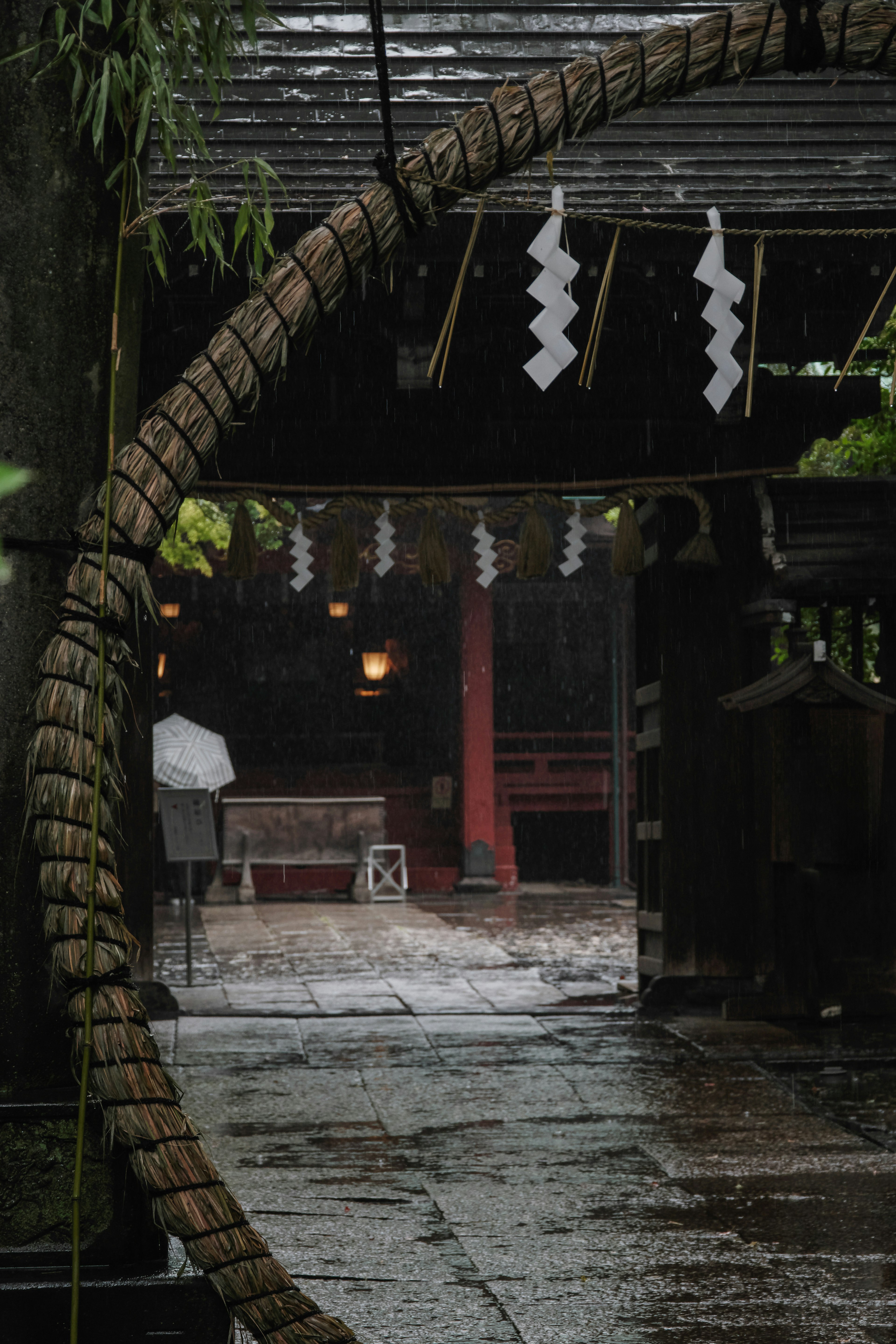 Entrada de un santuario adornada con un gran anillo de paja y decoraciones blancas bajo la lluvia