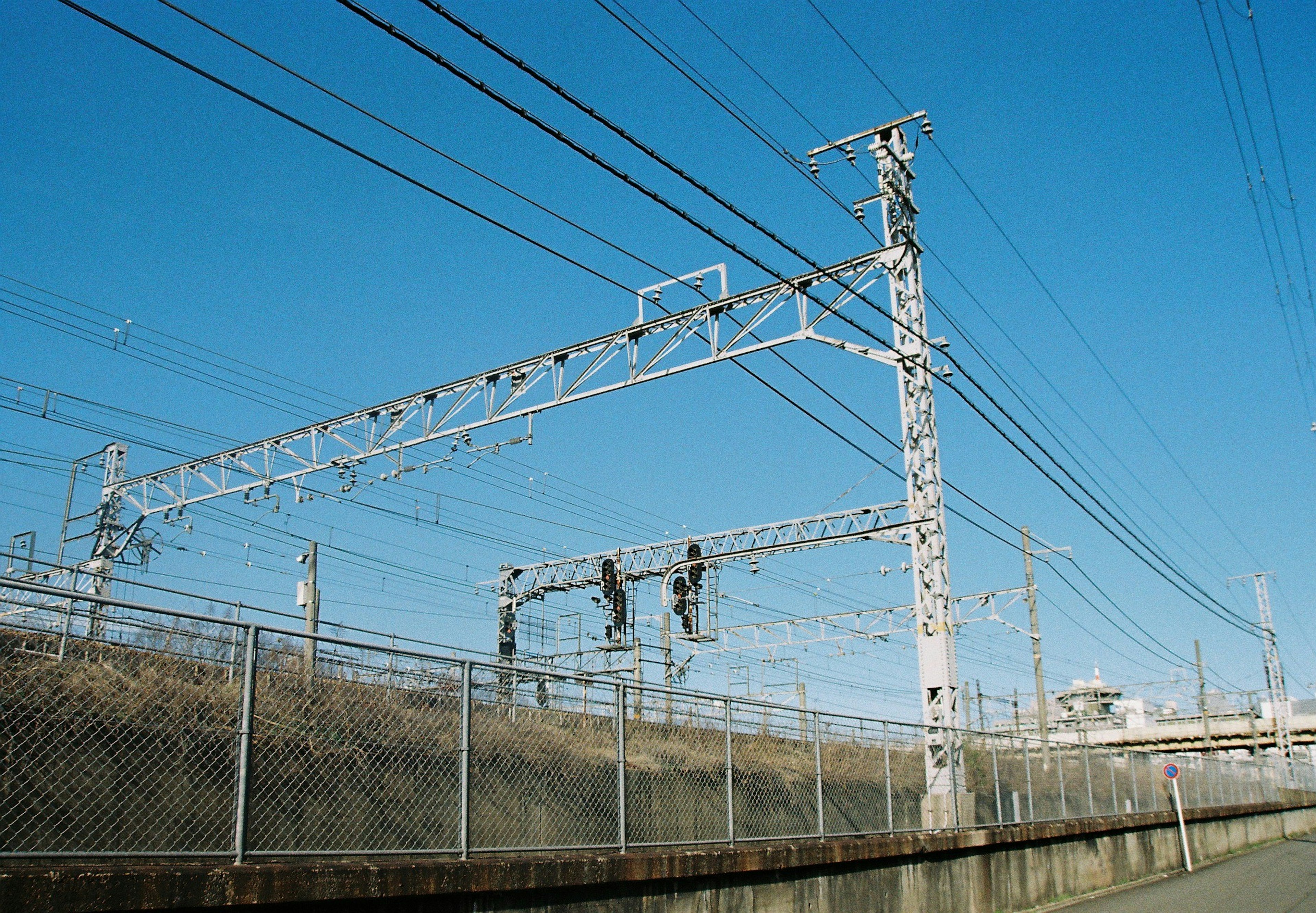 青空の下で見える鉄道の架線とフェンス