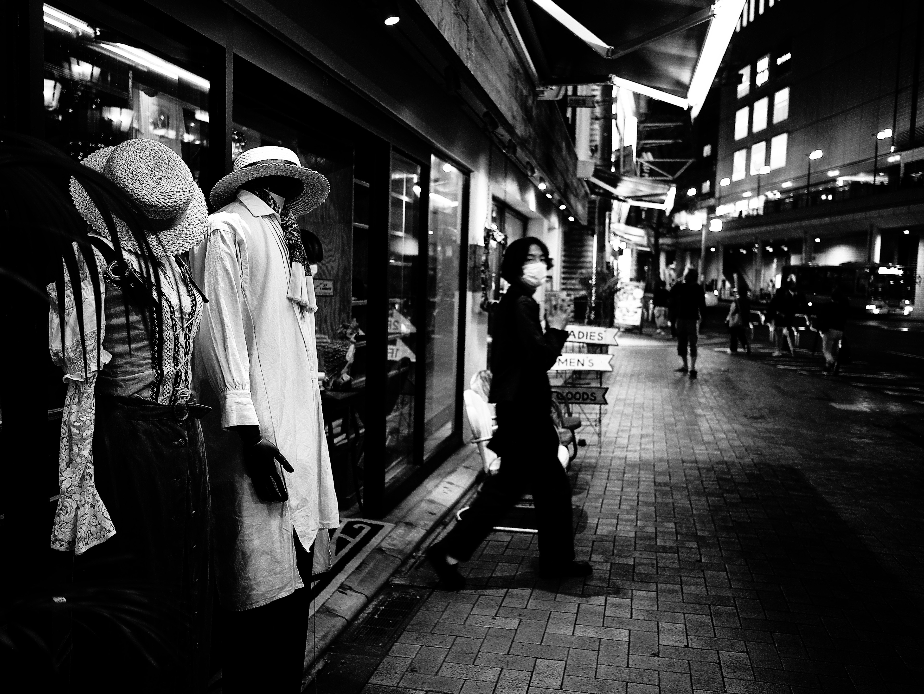 Scène de rue en noir et blanc avec des mannequins et une personne marchant