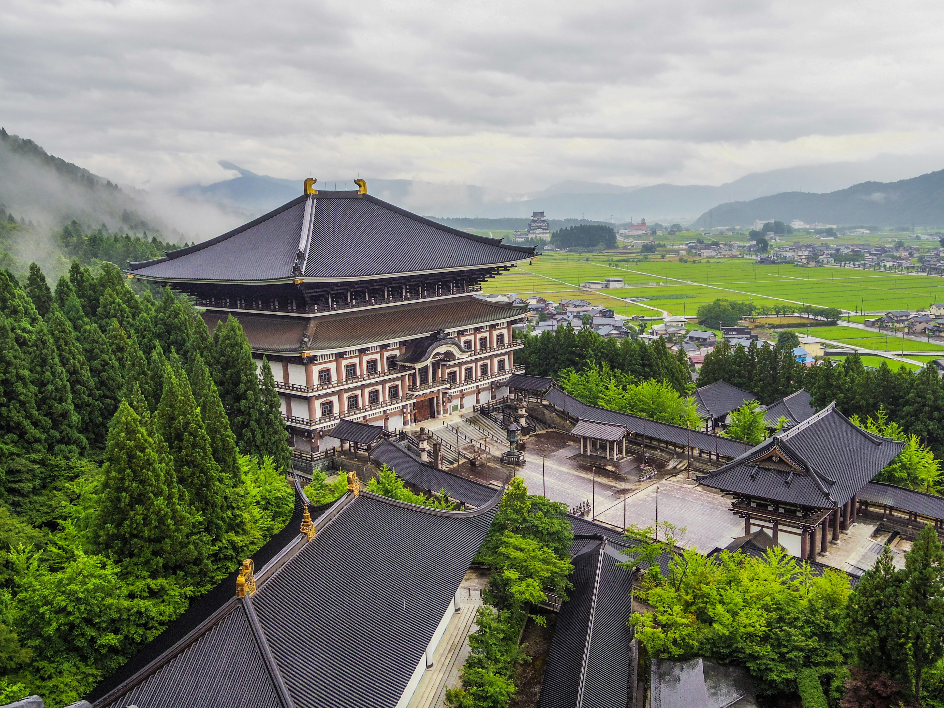 Ein großer Tempel umgeben von Grün mit einem bewölkten Himmel und Bergen im Hintergrund