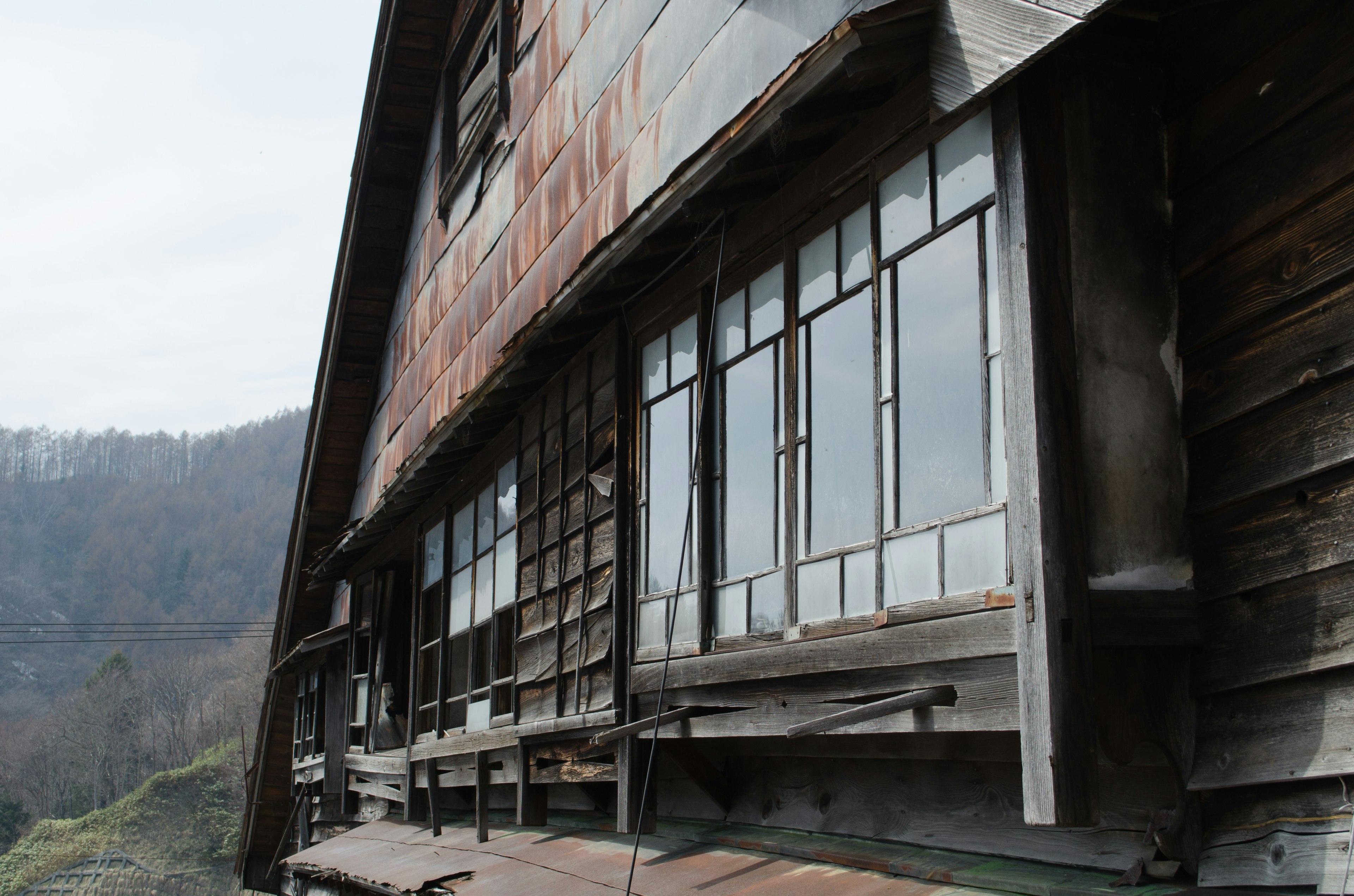 Side view of an old wooden house with distinctive windows and a mountain landscape in the background