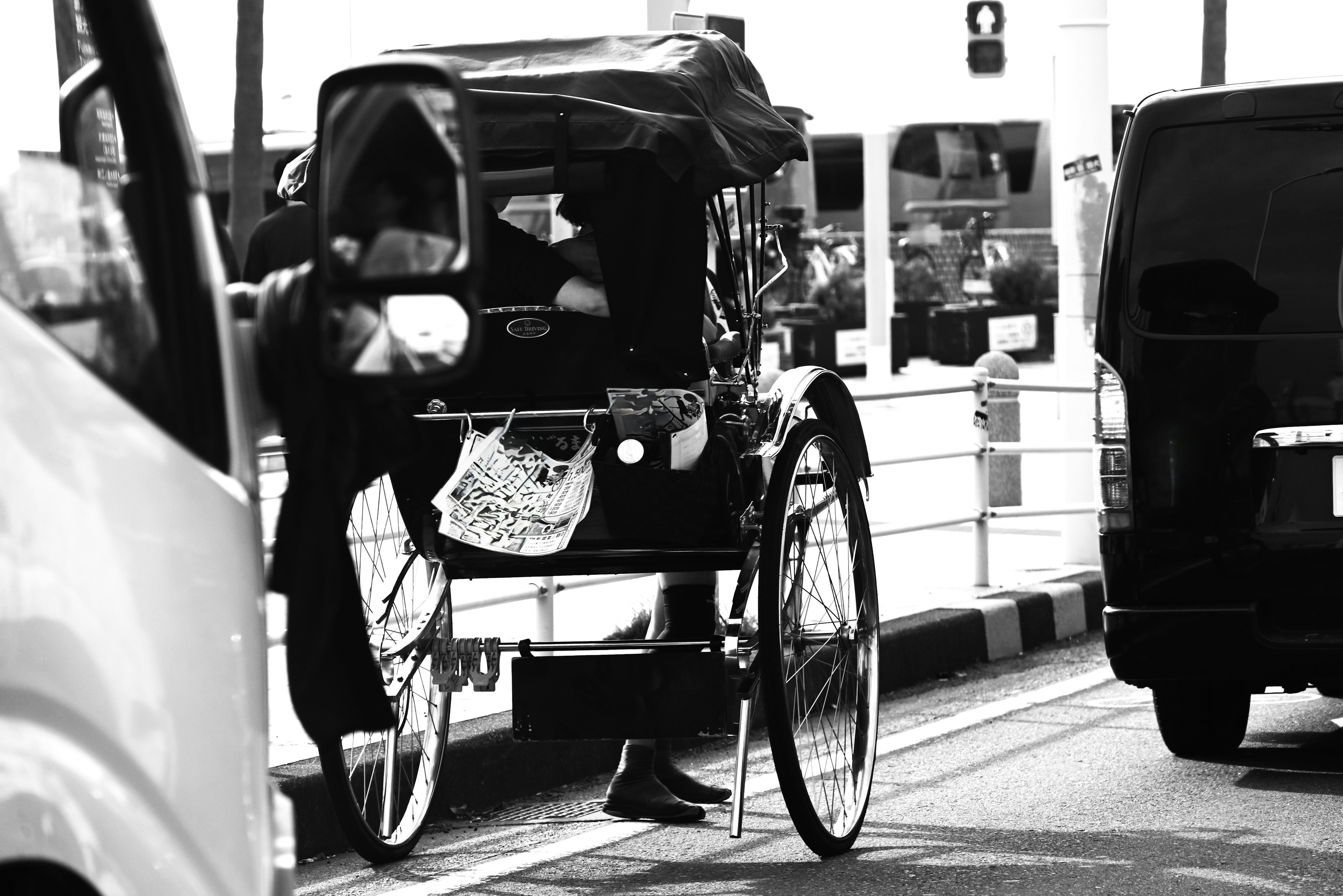 A rickshaw in black and white on a busy street with the driver boarding