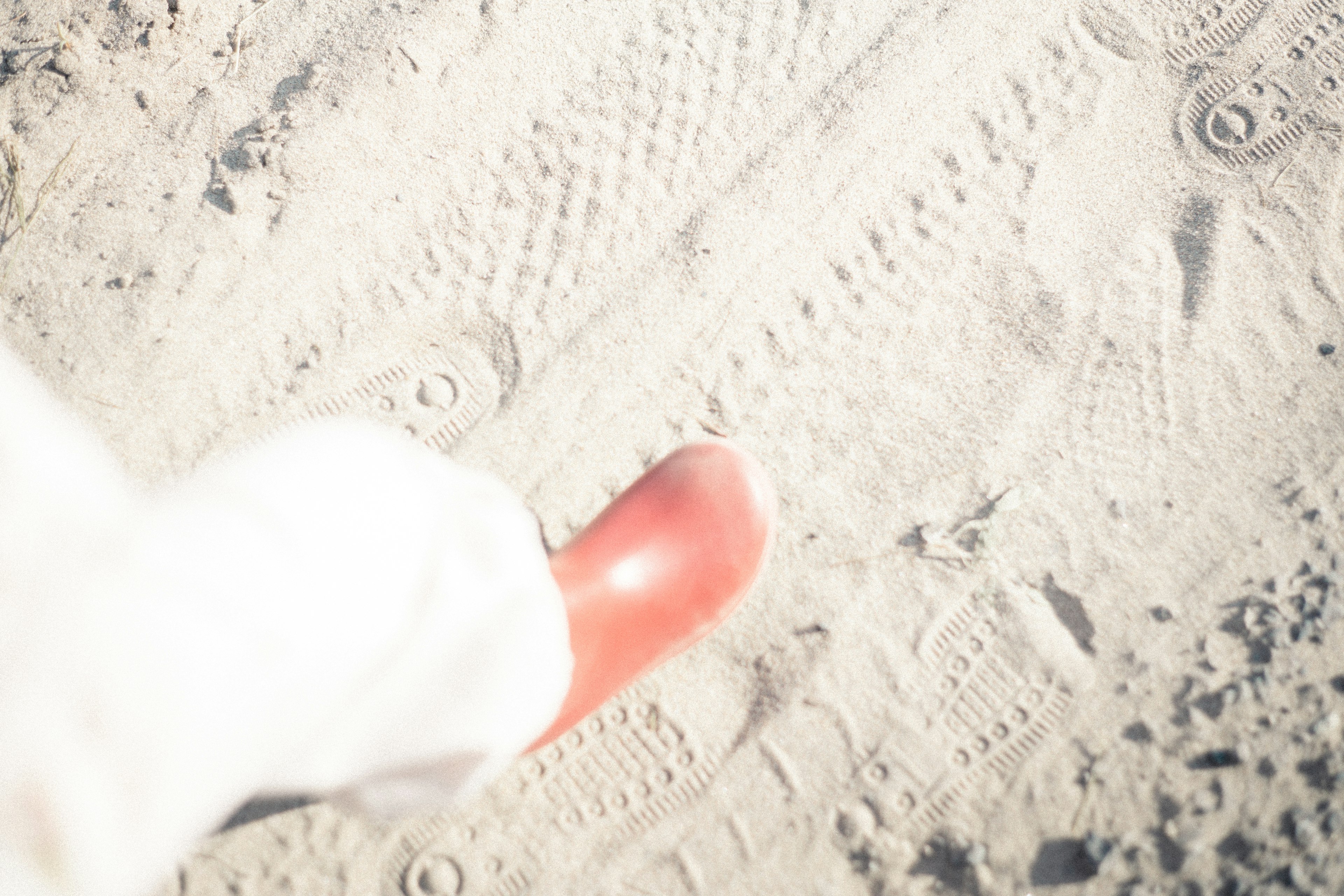 A person in white clothing walking on sand wearing red shoes