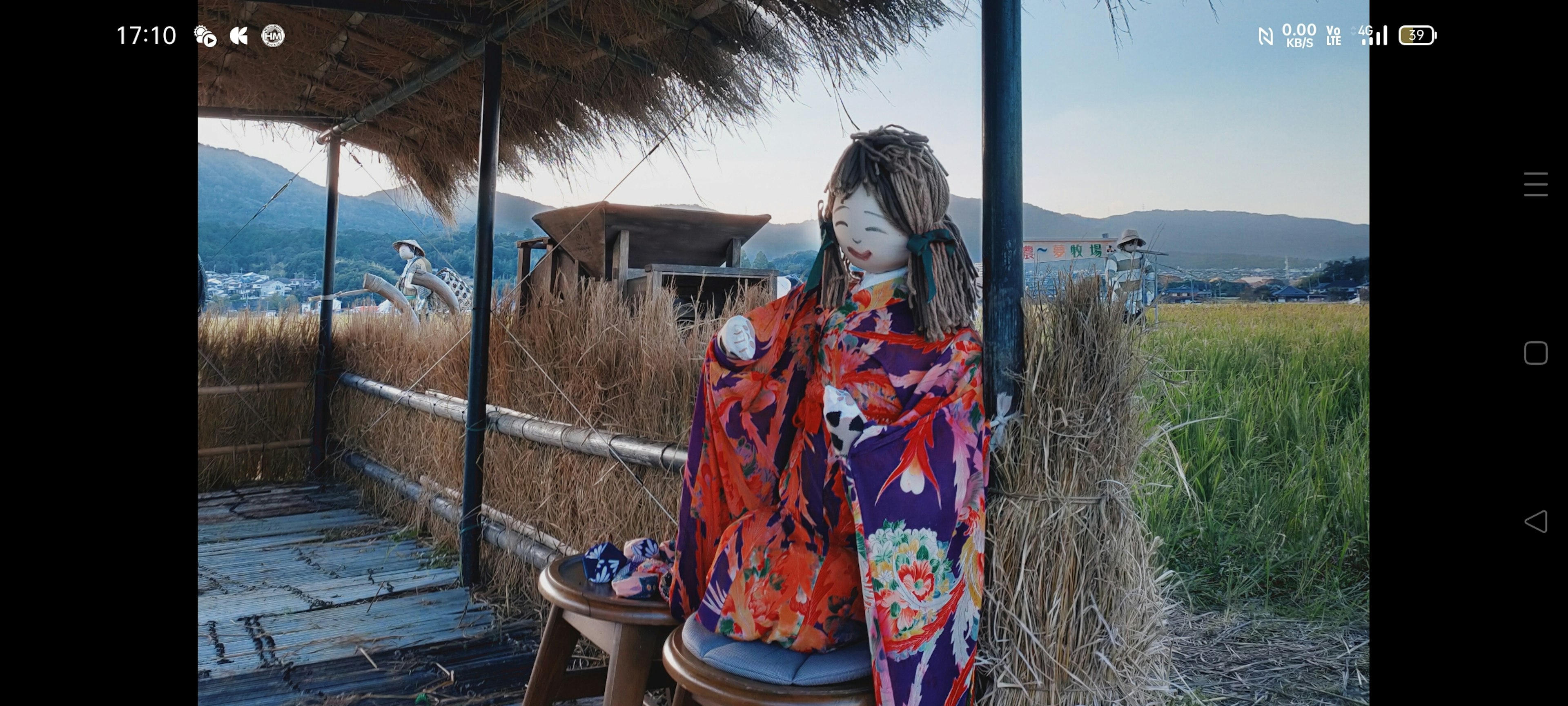 Una mujer en kimono colorido sentada frente a una cabaña de paja rodeada de hierba