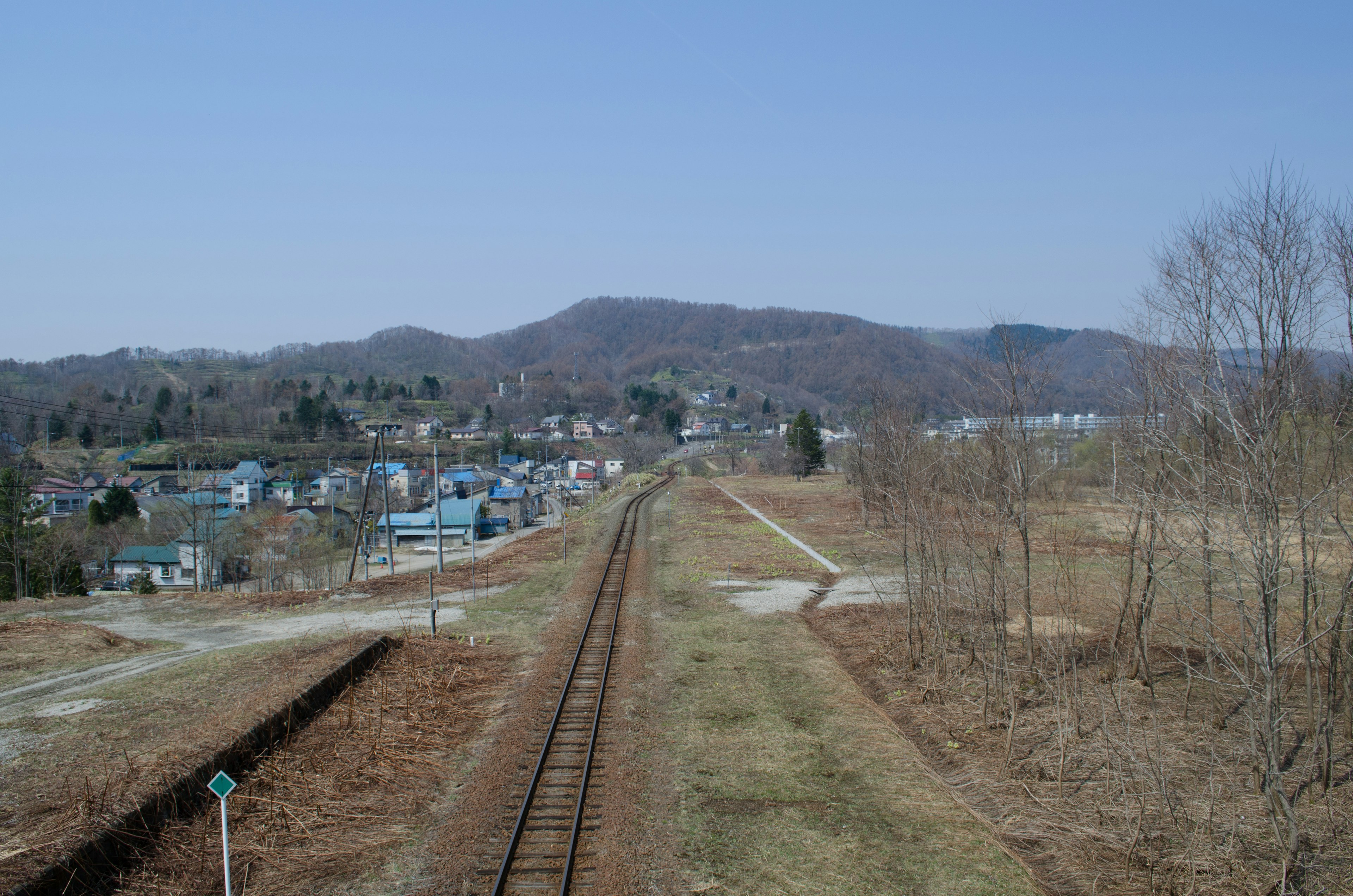 Paesaggio rurale con binari ferroviari sotto un cielo blu chiaro e montagne lontane