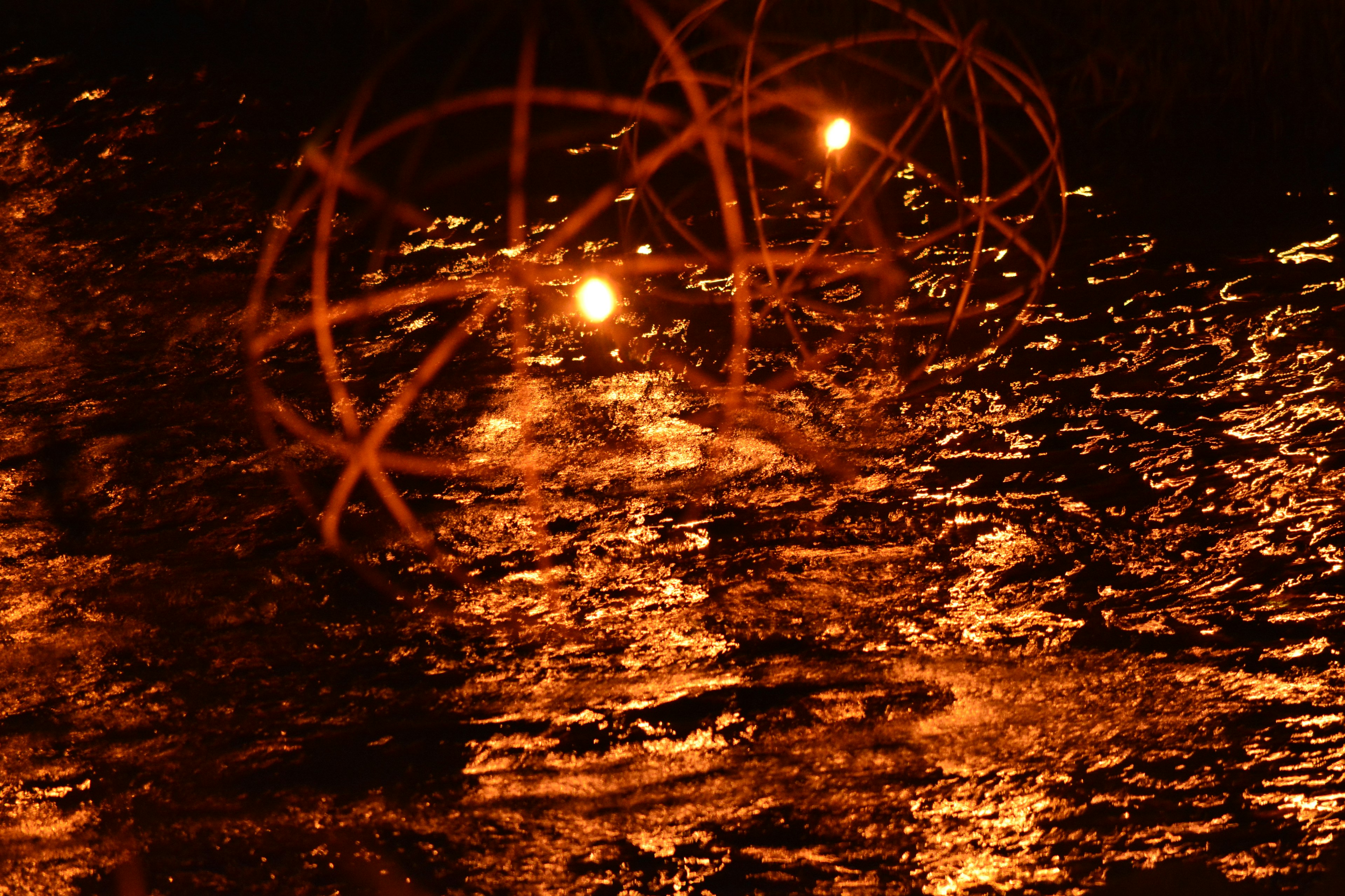 Vista nocturna de luces naranjas reflejándose en el agua con objetos esféricos