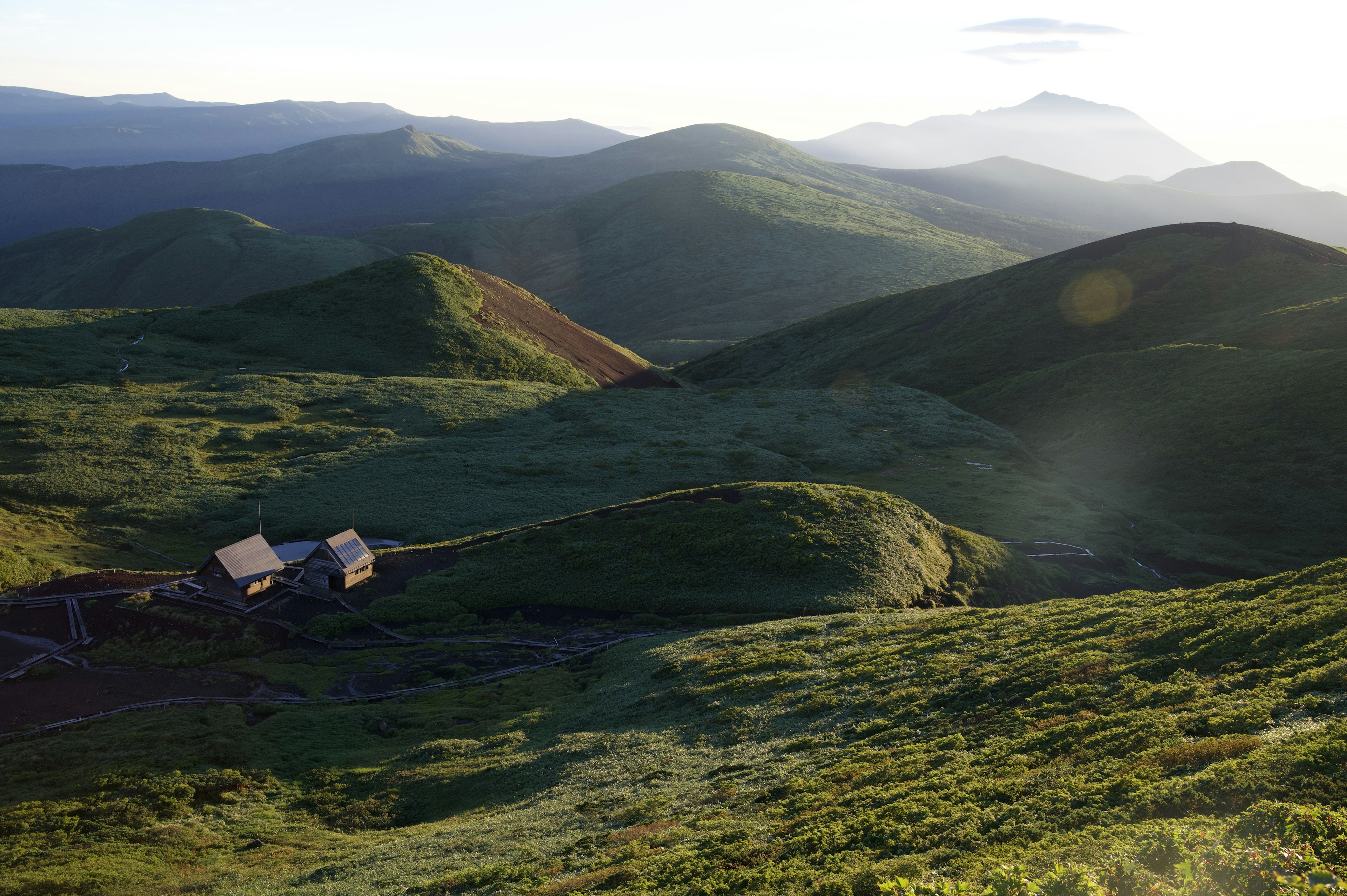 Paisaje escénico con colinas verdes onduladas y montañas distantes con una pequeña cabaña