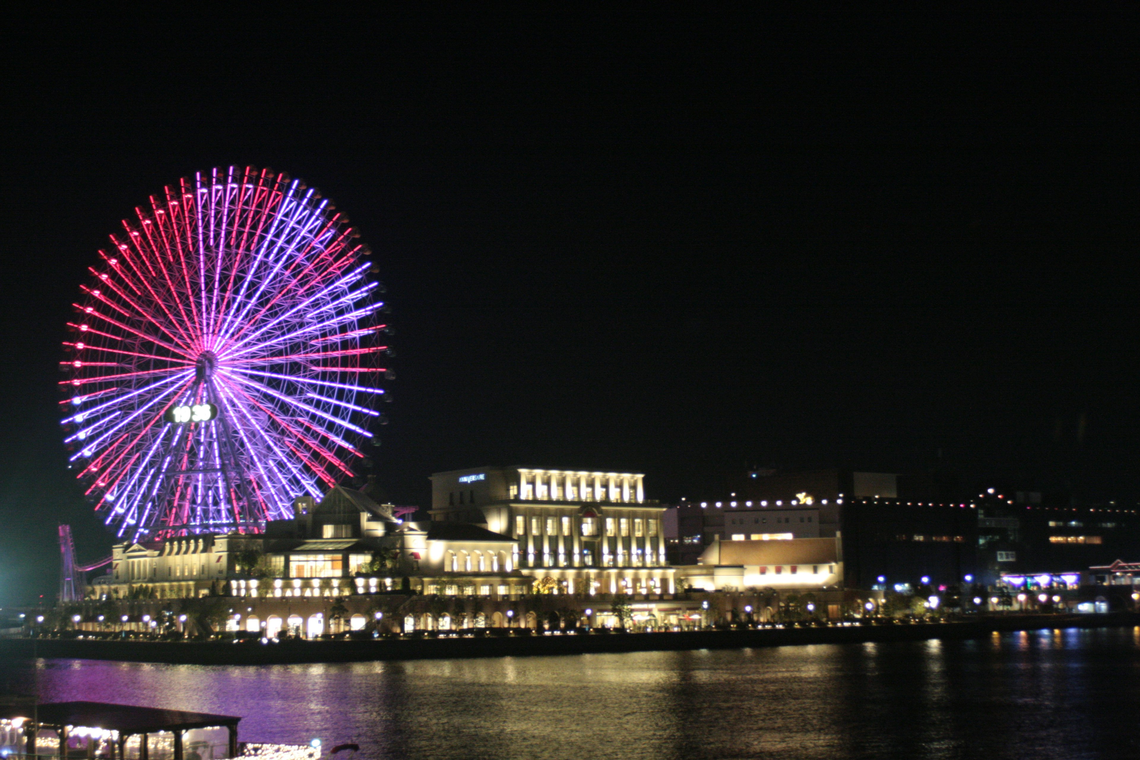 Nighttime view of a colorful Ferris wheel and waterfront buildings