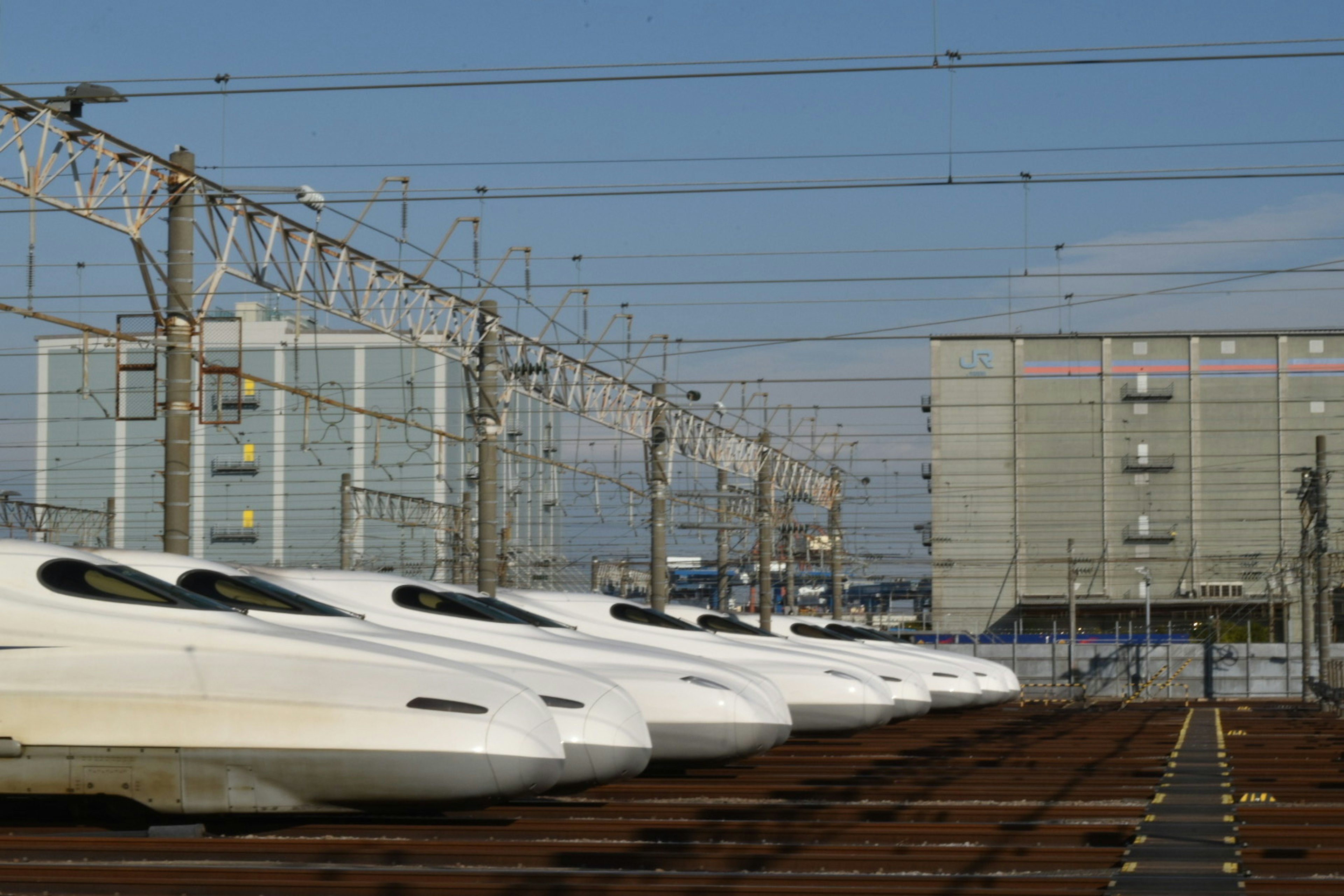 Các đoàn tàu Shinkansen xếp hàng tại ga với bầu trời xanh trong và dây điện trên cao