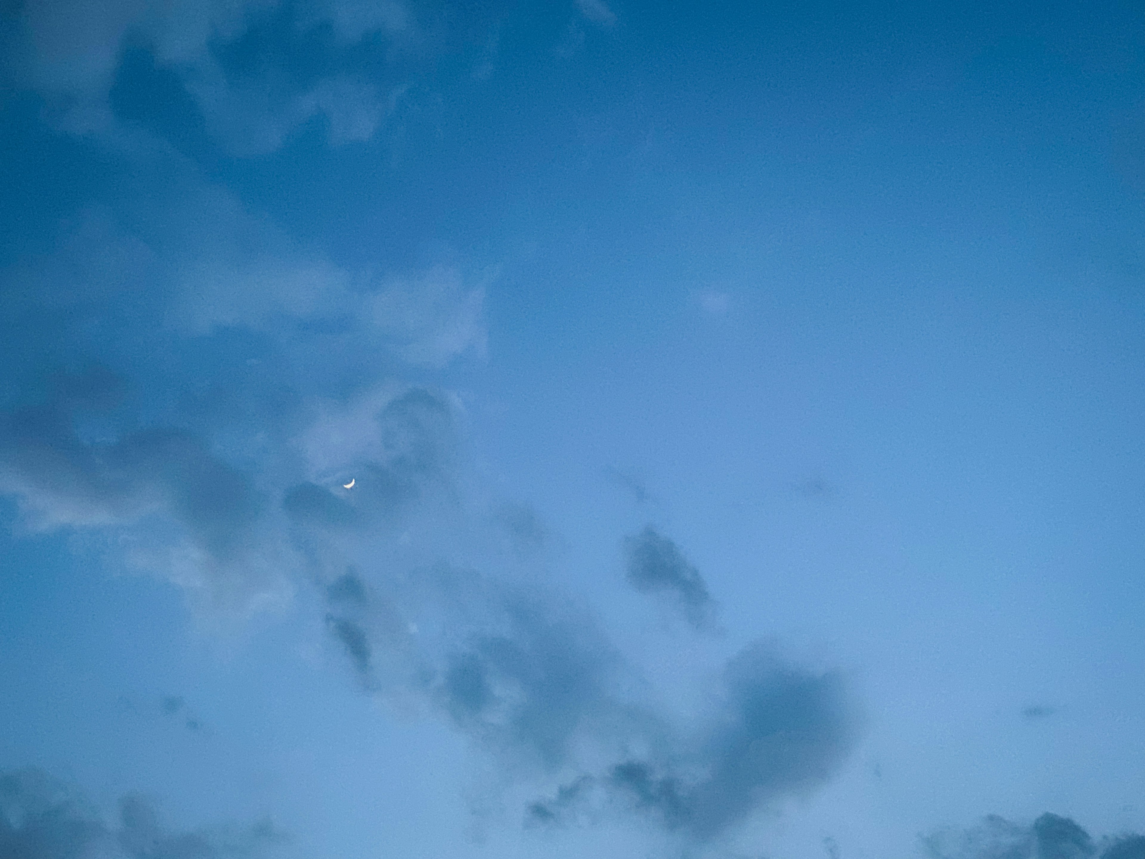 A clear blue sky with clouds and a small moon appearing