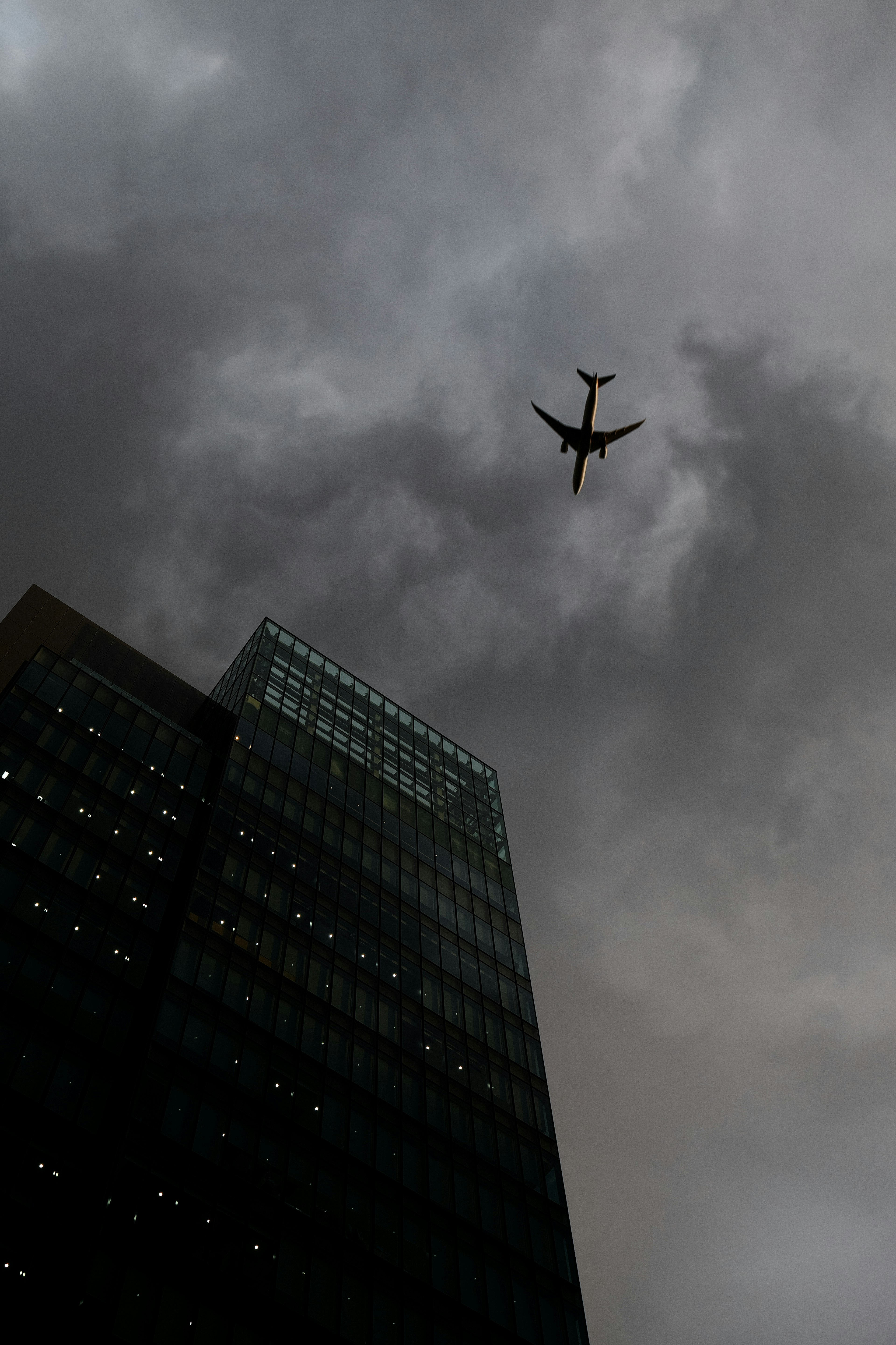 Silhouette of an airplane flying above a tall building under dark clouds