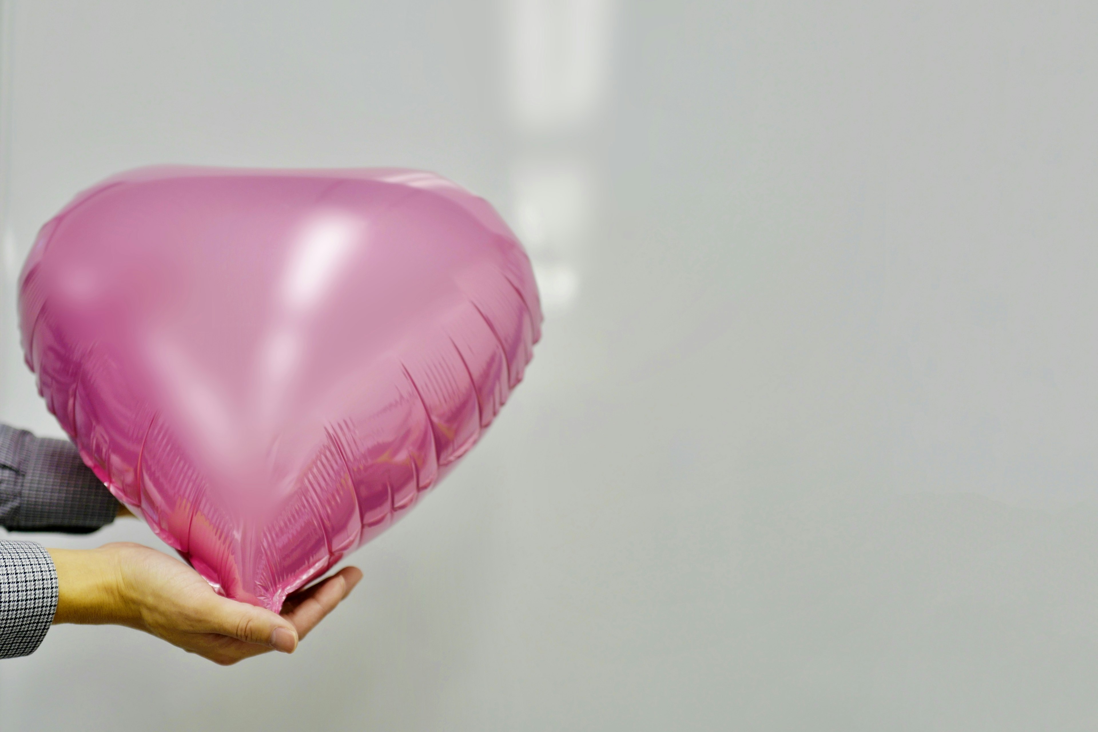 A hand holding a pink heart-shaped balloon