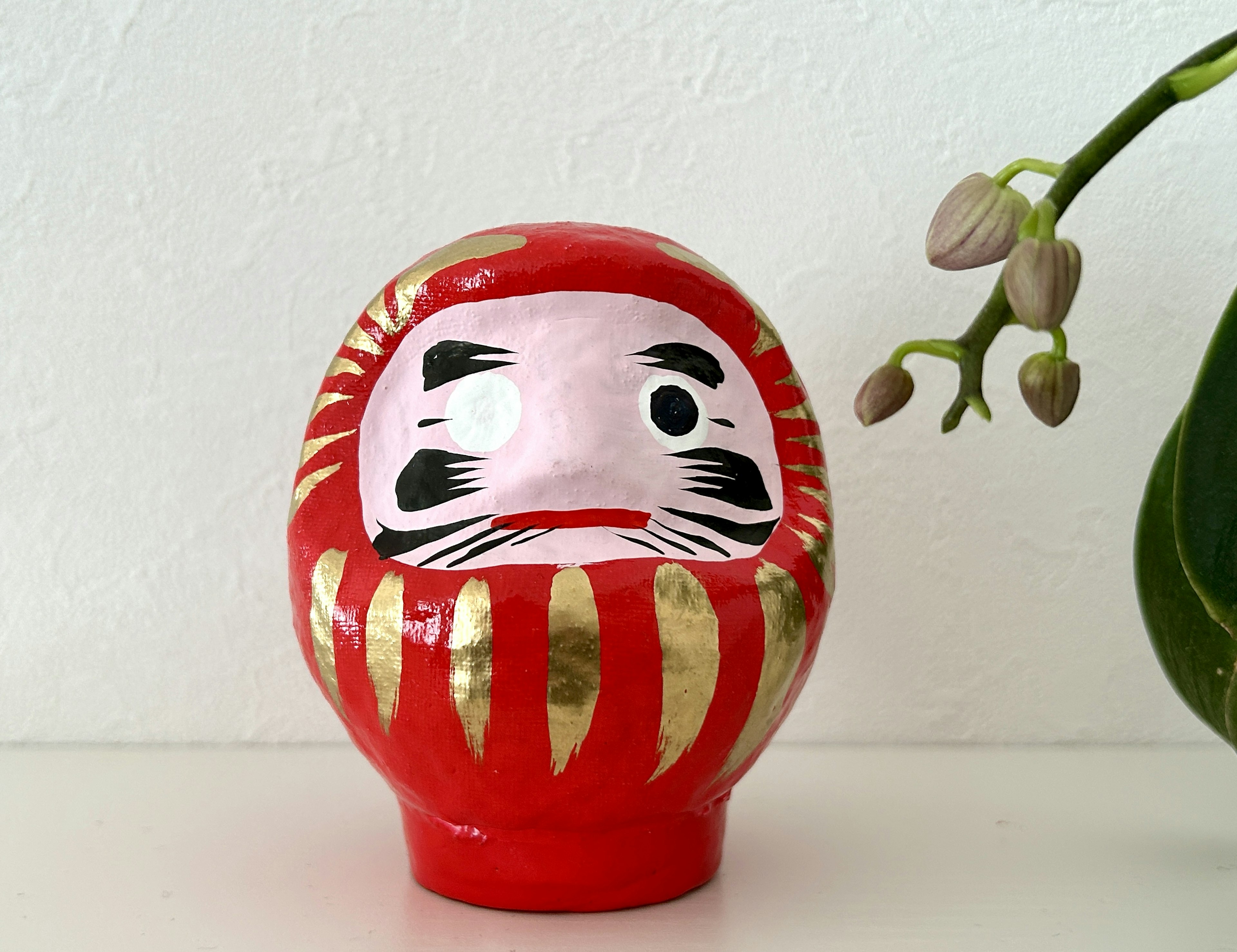 Patung boneka Daruma merah dengan latar belakang tanaman