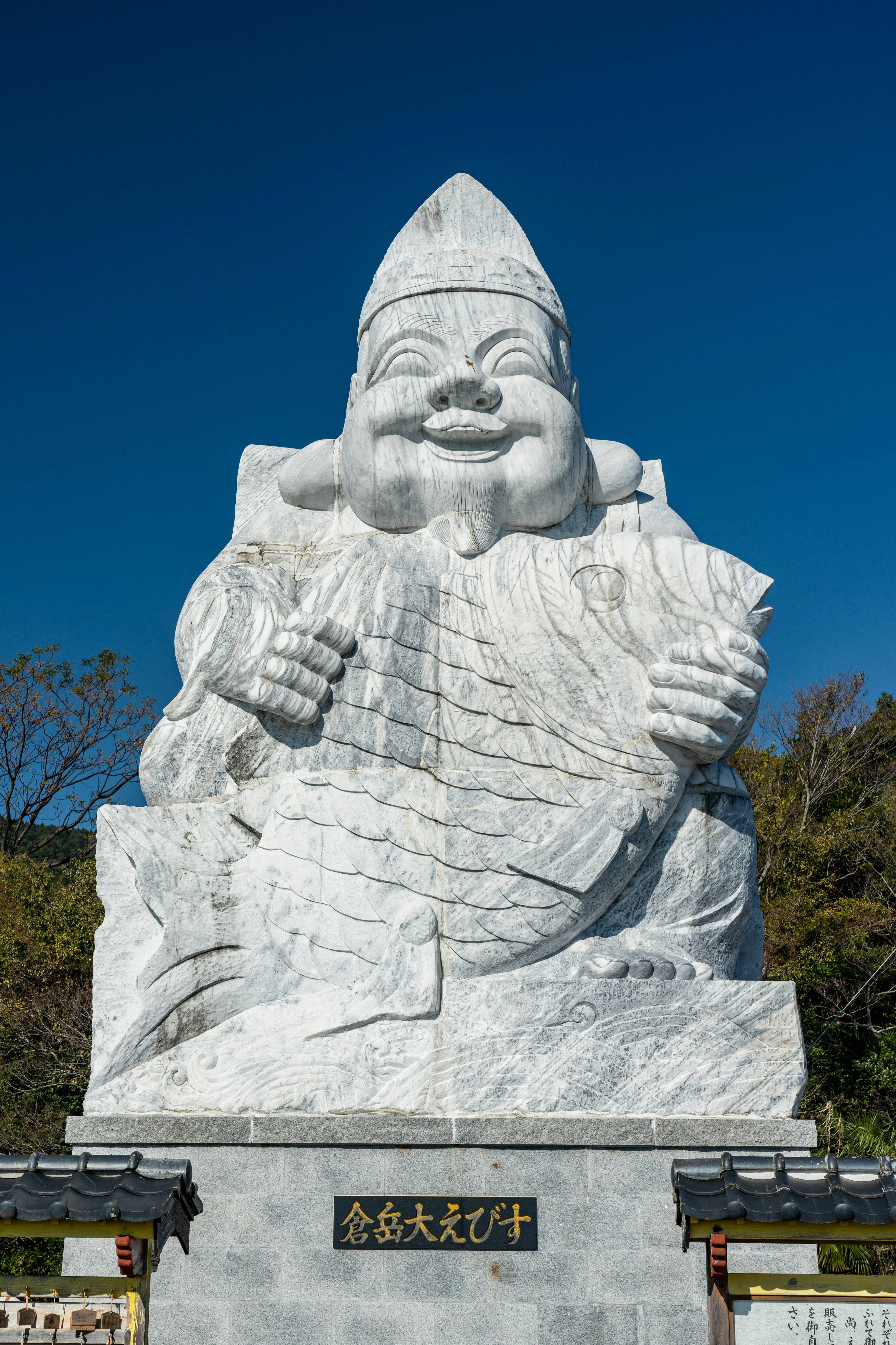 Grande statue en pierre blanche d'une divinité souriante portant une tenue traditionnelle