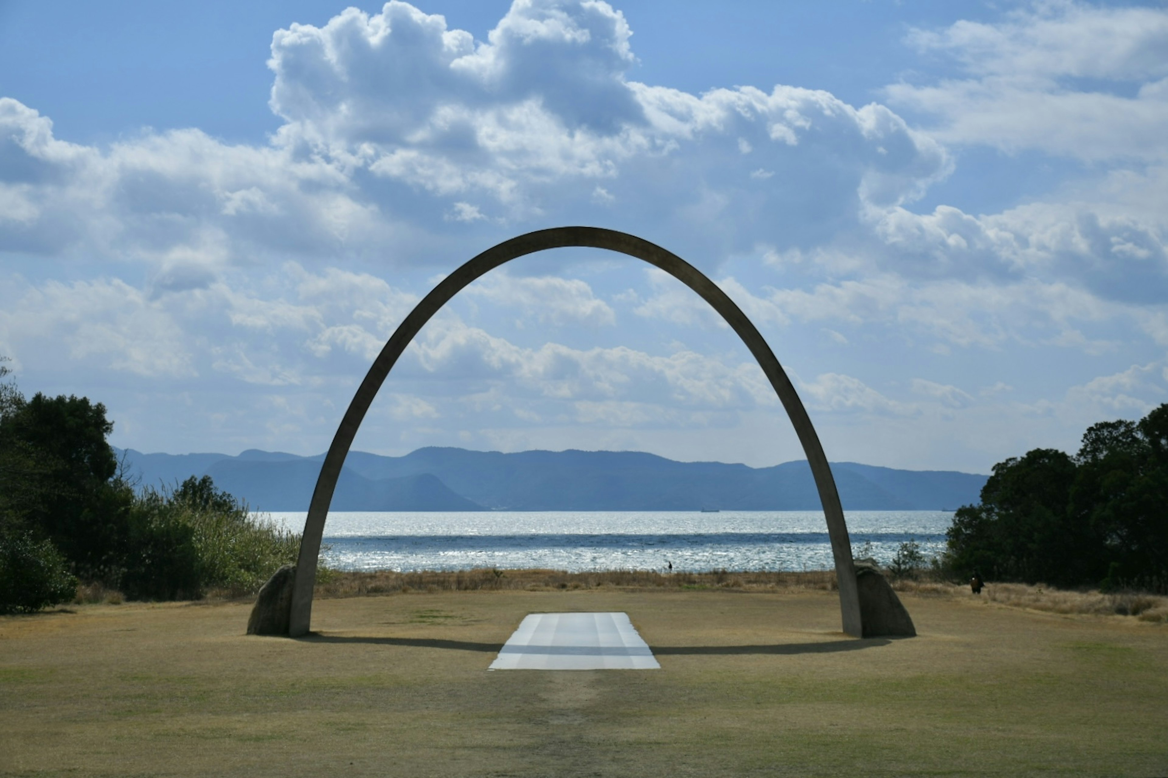 Arch-shaped sculpture against a blue sky and lake