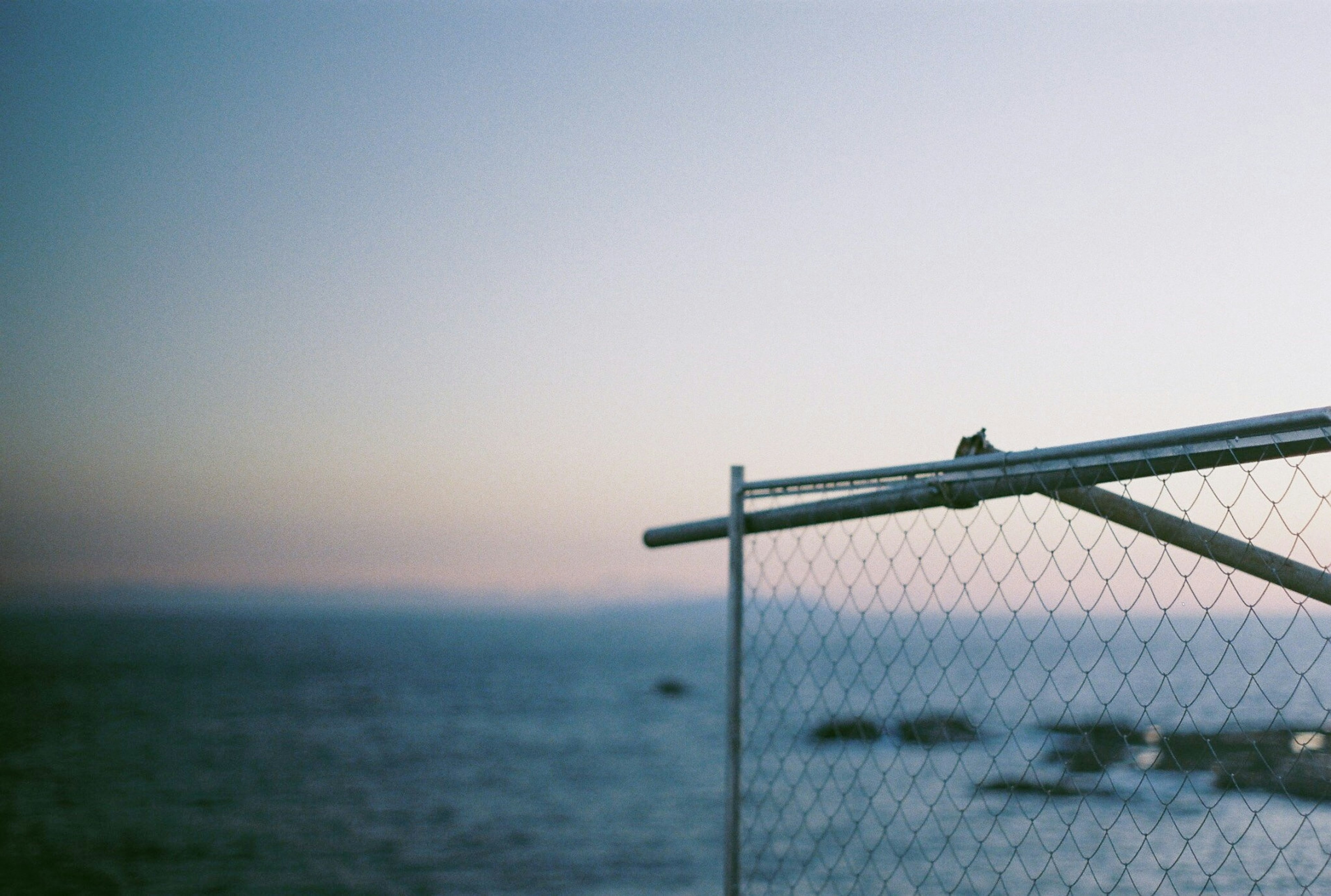 Part of a fence overlooking the sea with a soft gradient sky