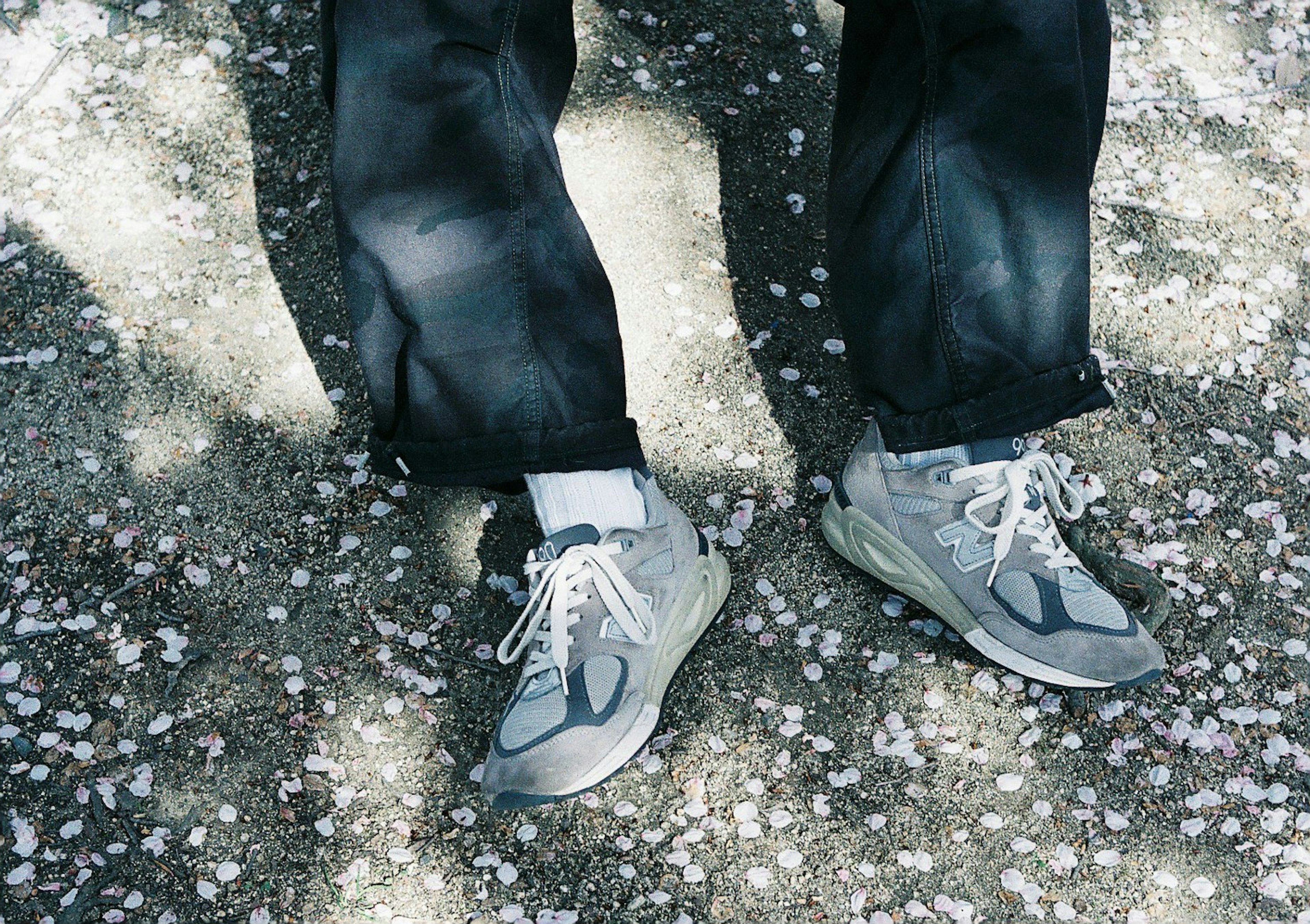 Feet wearing gray sneakers and black pants on a gravel surface