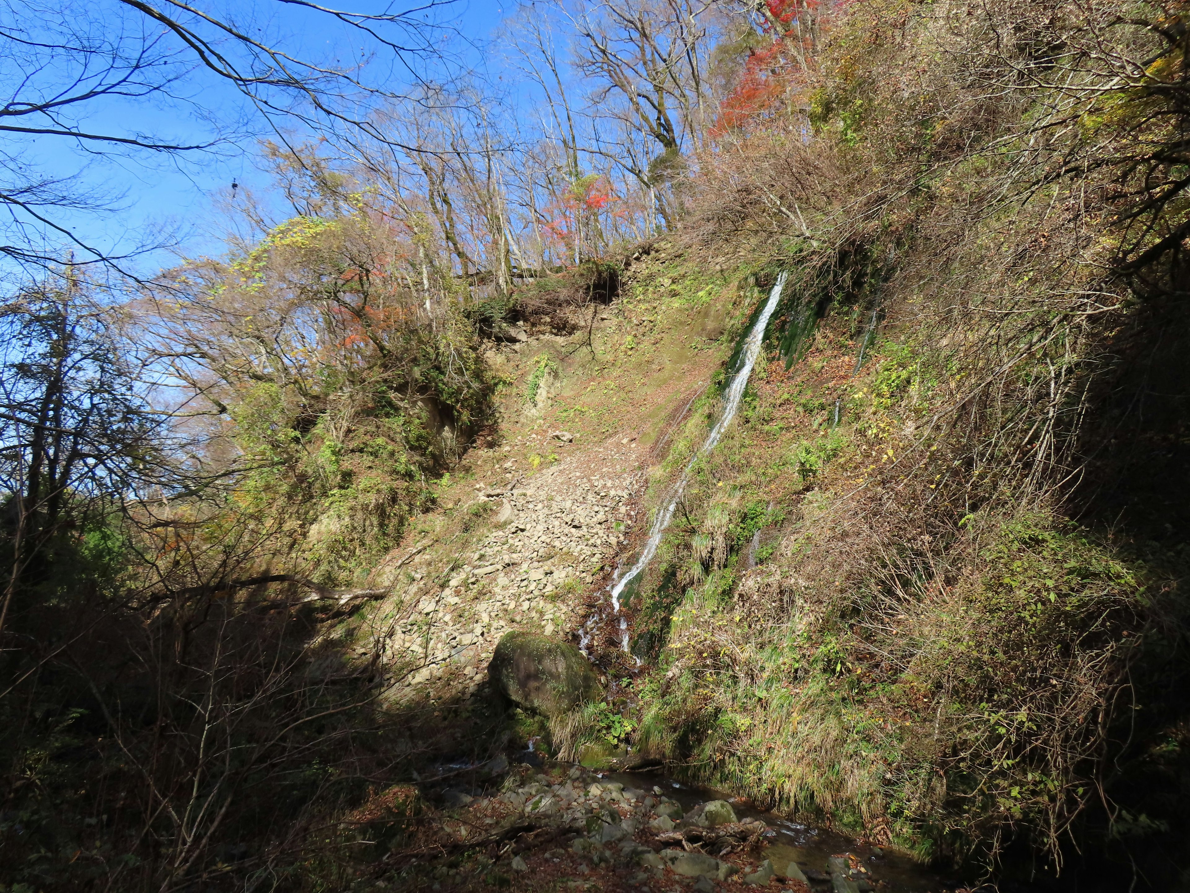 Ladera frondosa con una pequeña cascada bajo un cielo azul