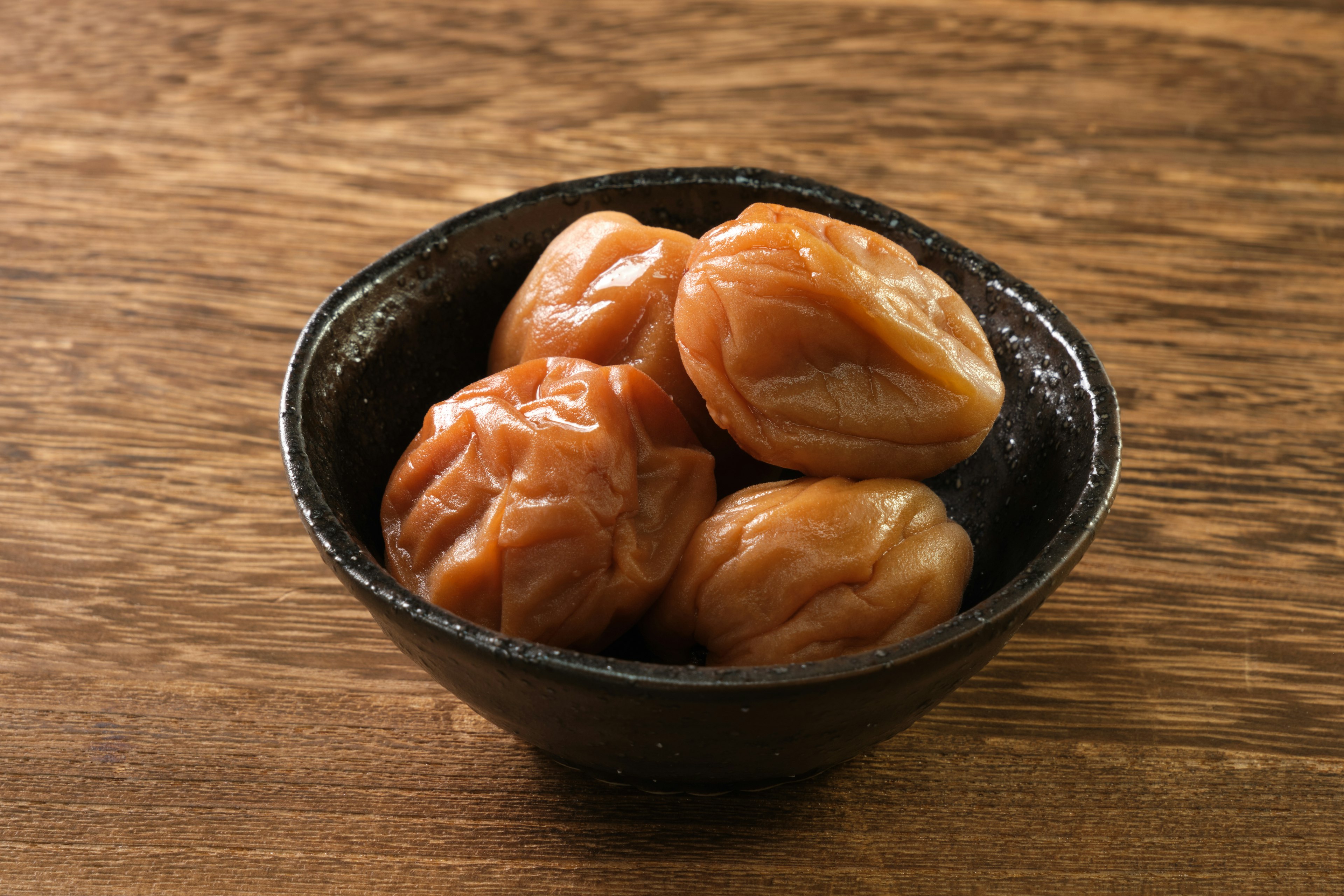 Plum pickles in a black bowl on a wooden surface