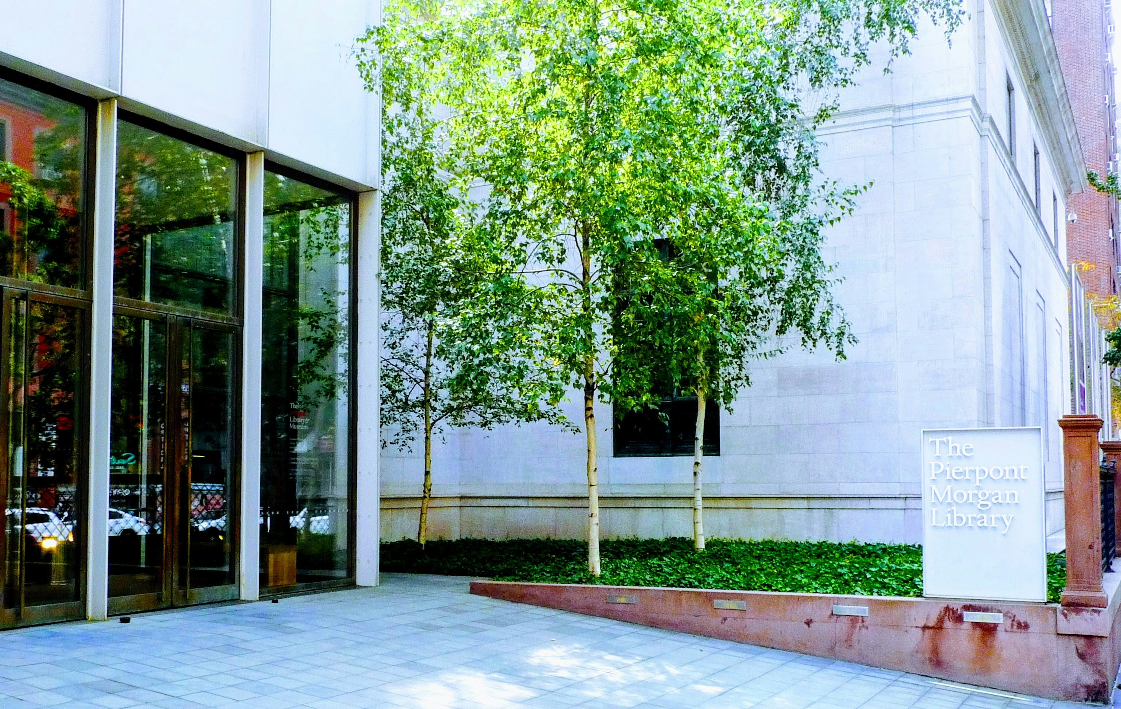 Entrada de un edificio moderno con árboles verdes y un camino de piedra bien pavimentado