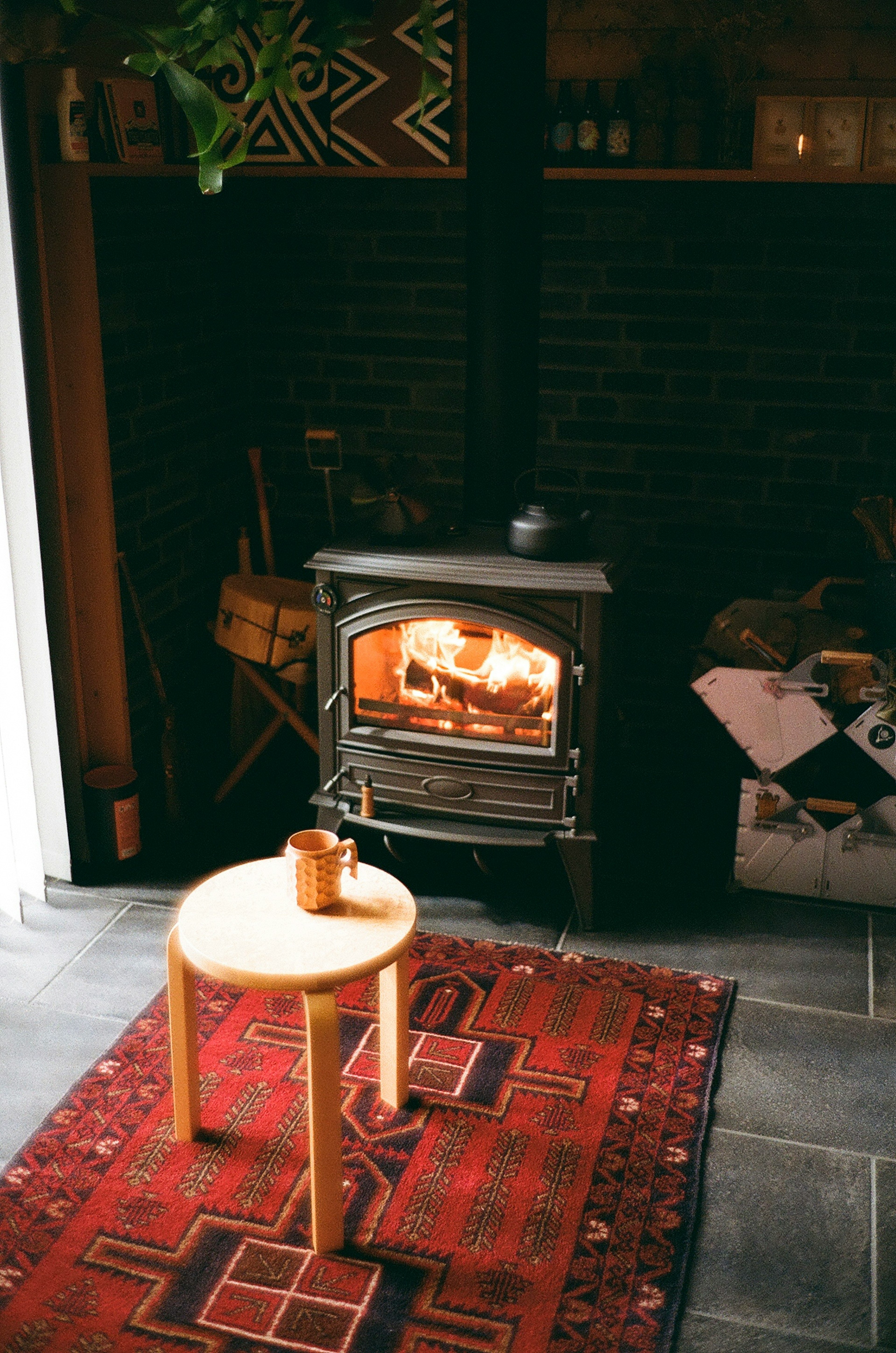 Tabouret en bois placé devant un poêle avec une tasse en céramique sur un tapis à motifs