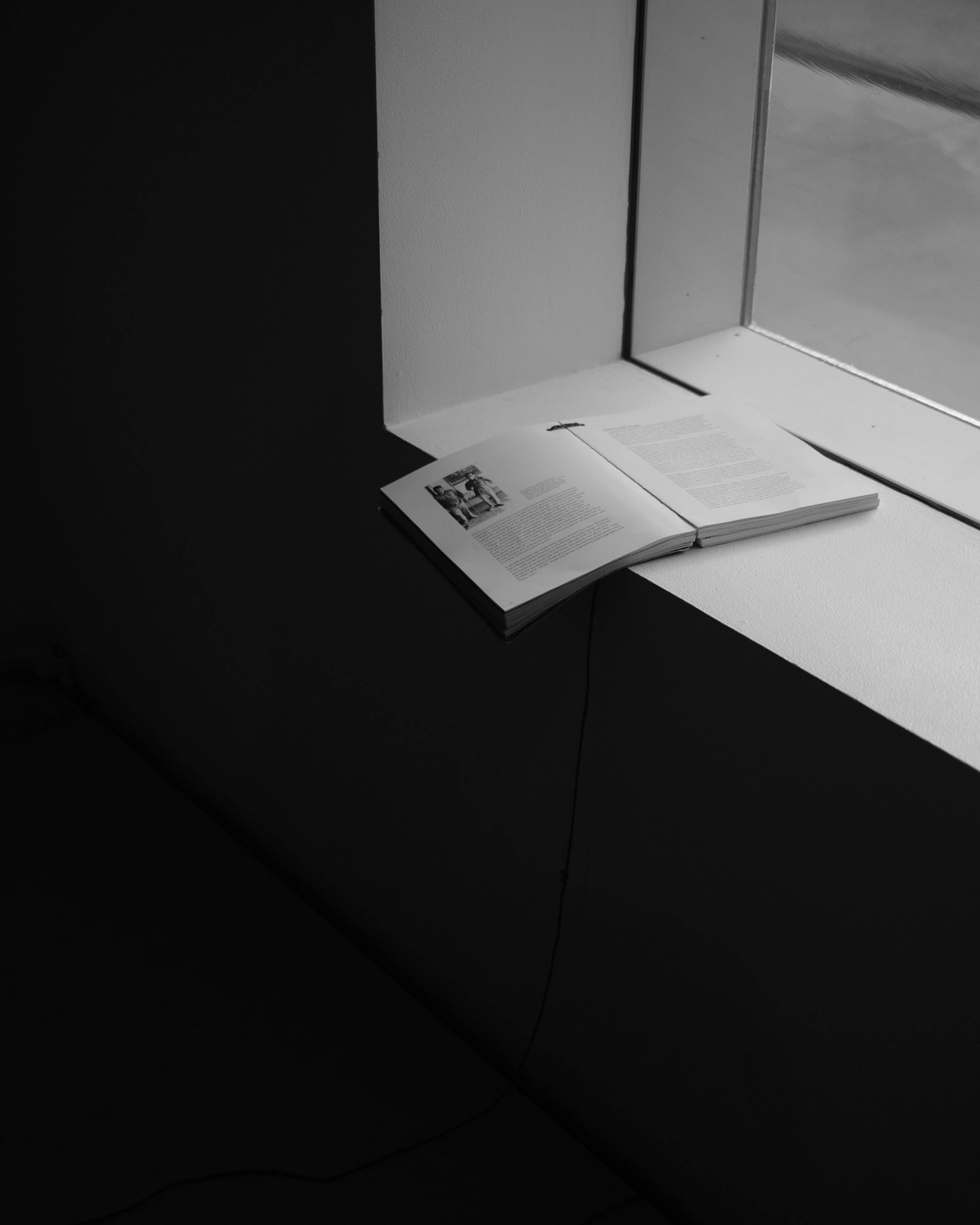 Black and white photo of an open book on a windowsill