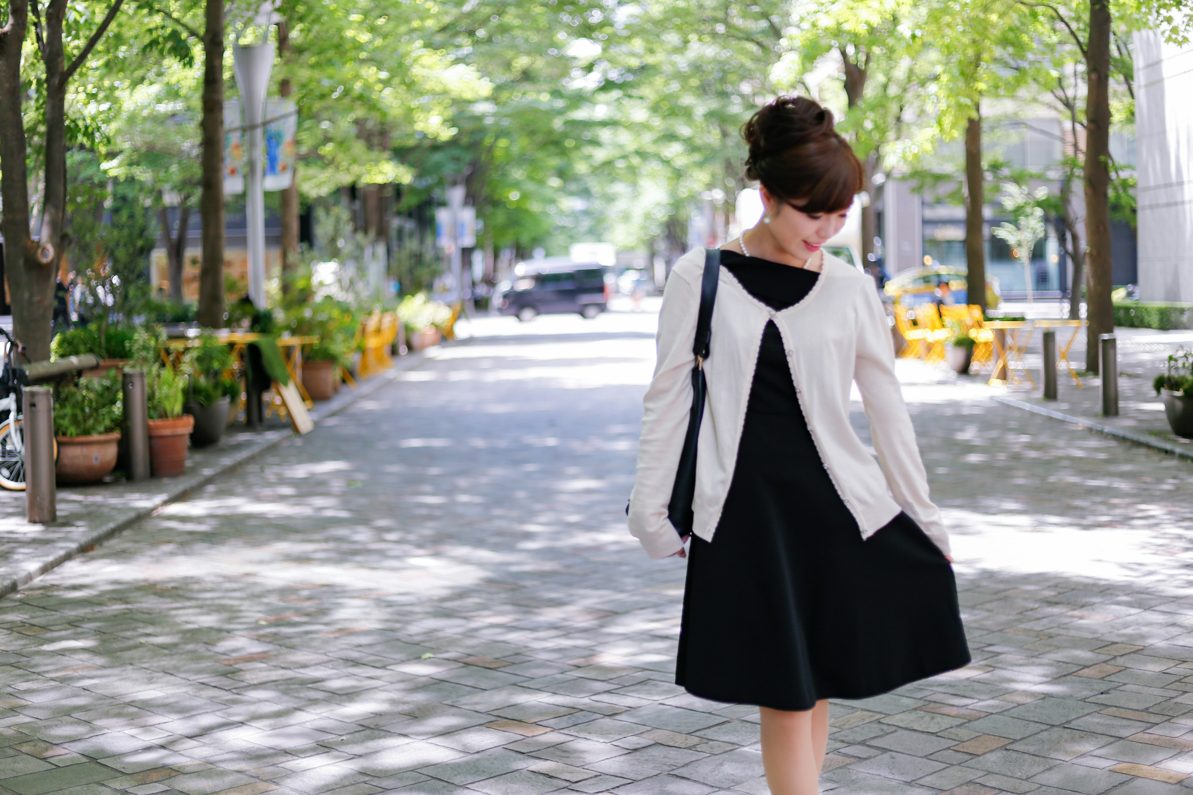 Une femme portant une robe noire et un cardigan blanc dans une scène de rue