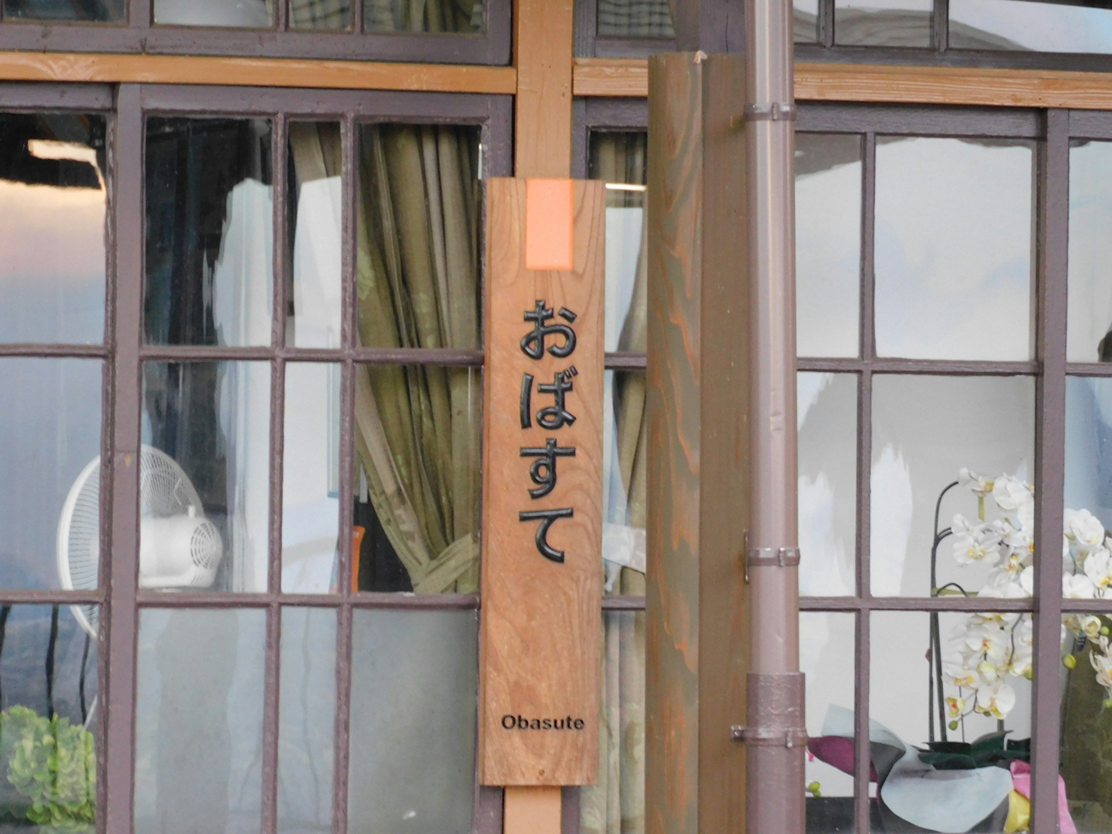 Holzschild mit dem Wort obasute und Fenstergestaltung