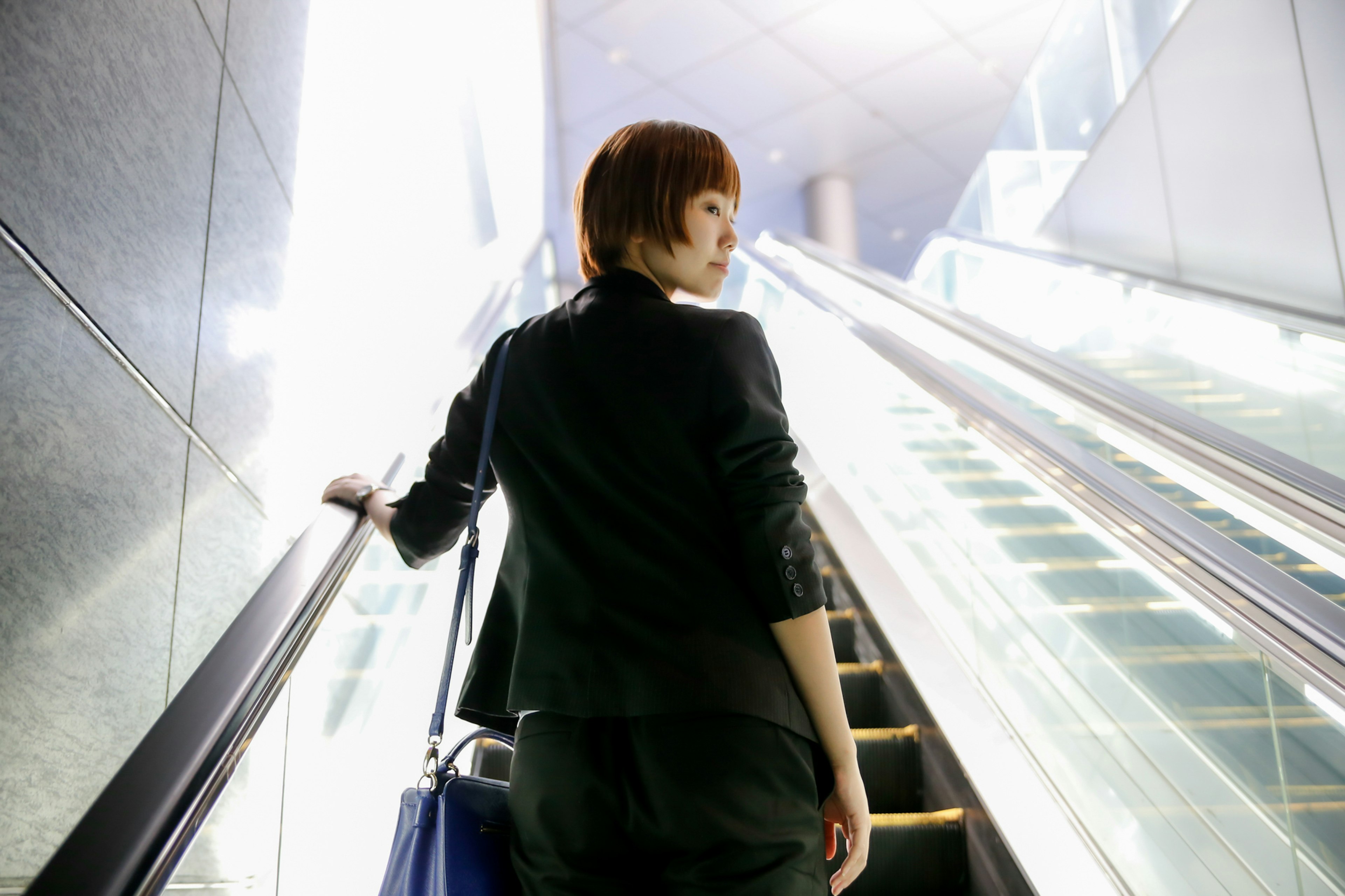 Woman in business attire ascending an escalator