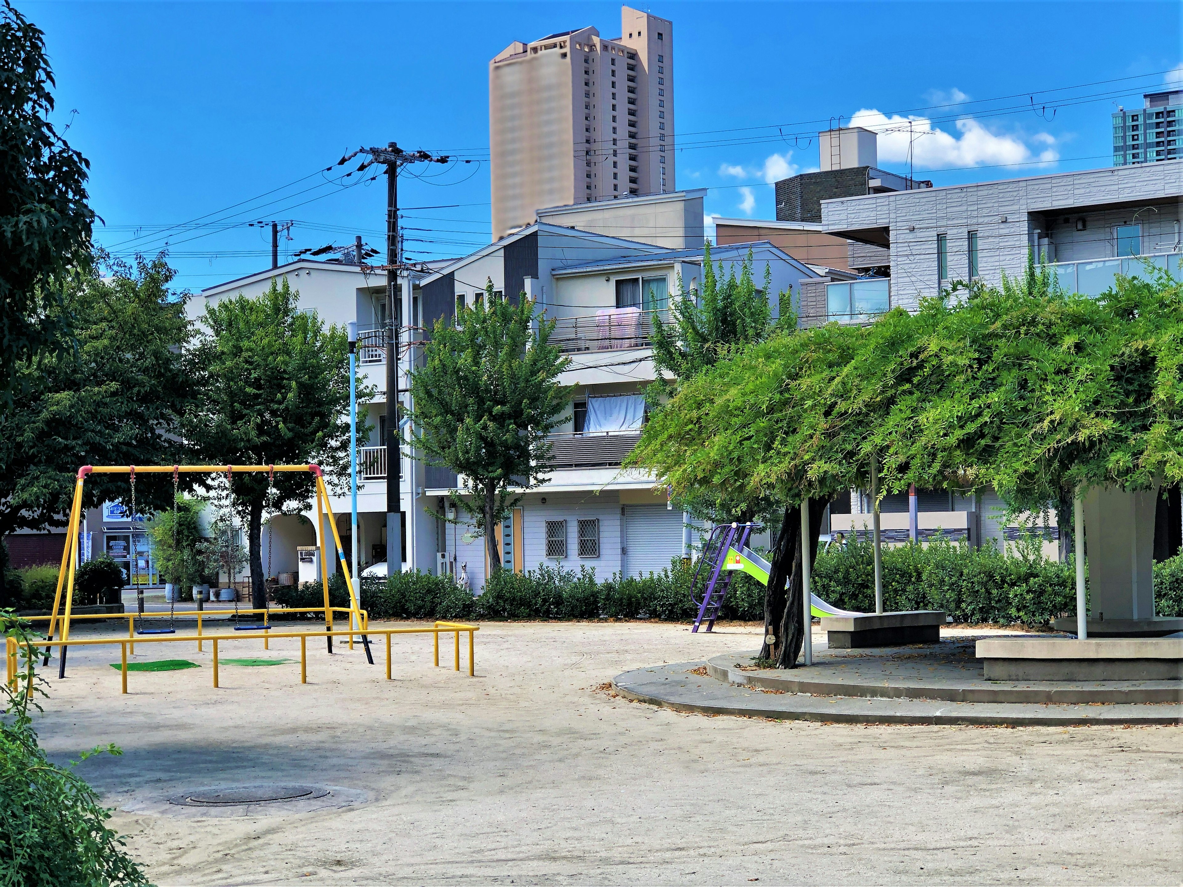 Park scene featuring a swing set and slide with high-rise buildings in the background