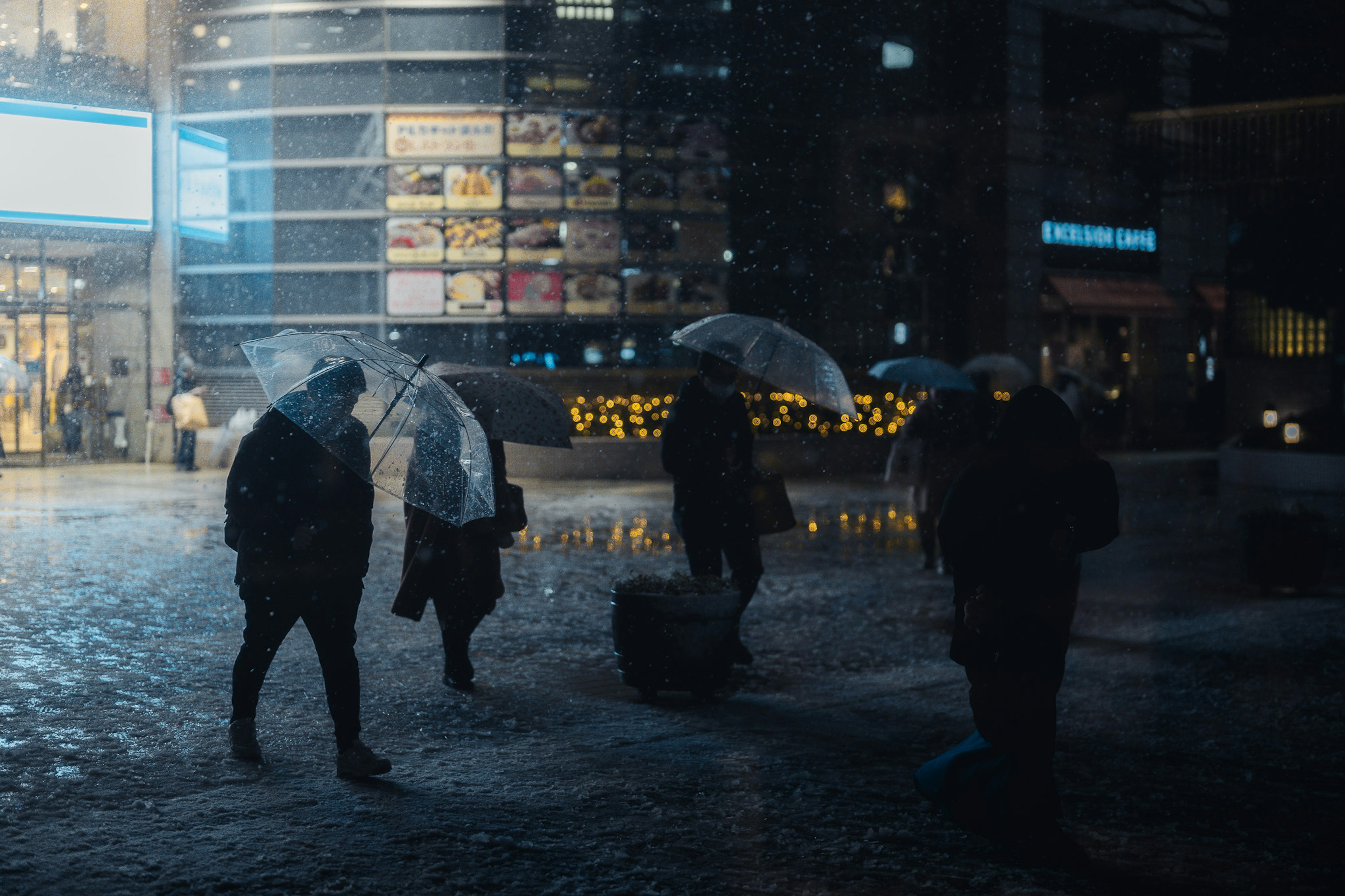 Silhouetten von Menschen, die bei Regen mit Regenschirmen gehen Stadtlichter, die sich in Pfützen spiegeln