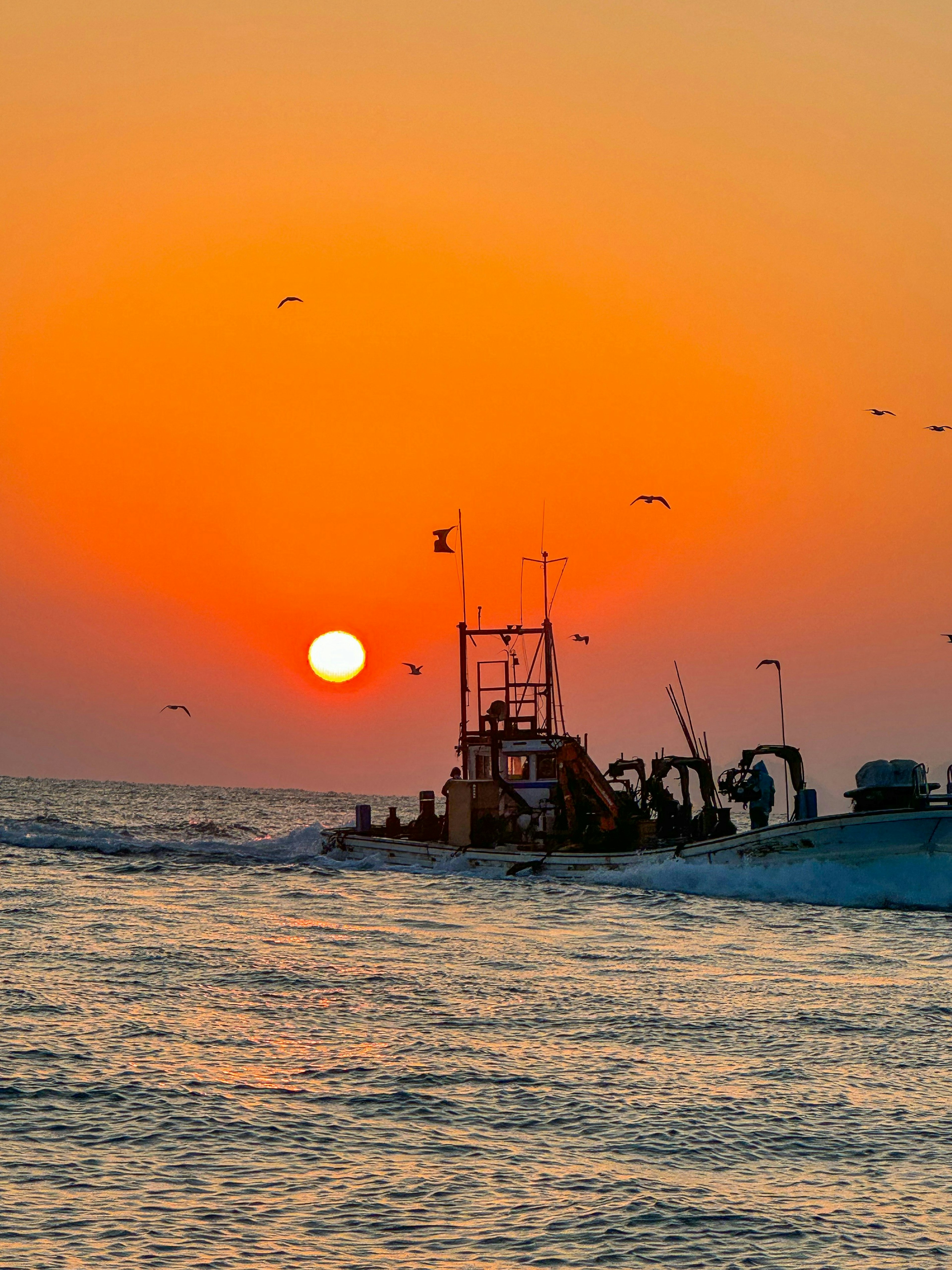 Fishing boat silhouetted against a vibrant sunset over the ocean