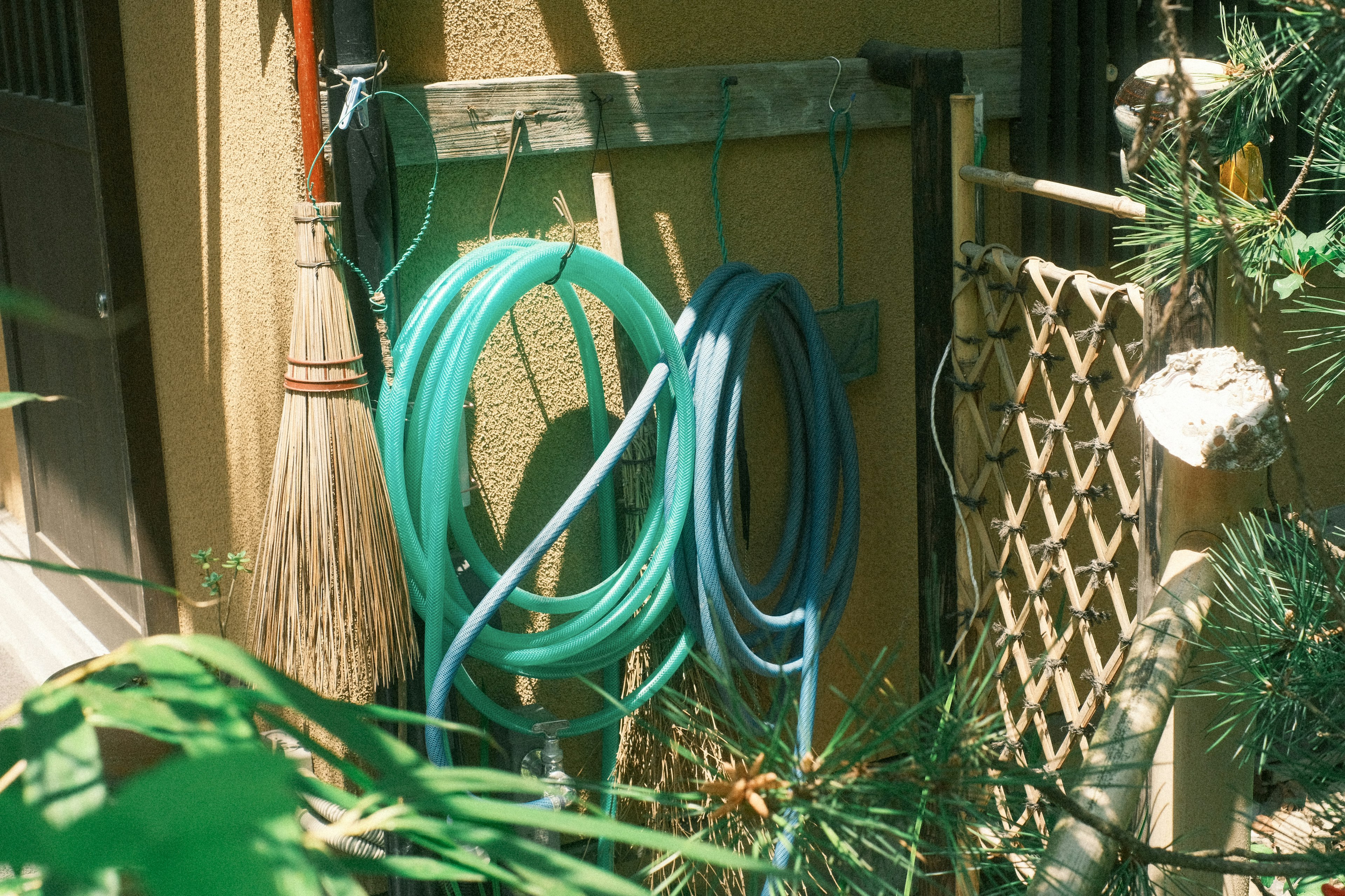 Green and blue hoses hanging on an exterior wall with a broom nearby