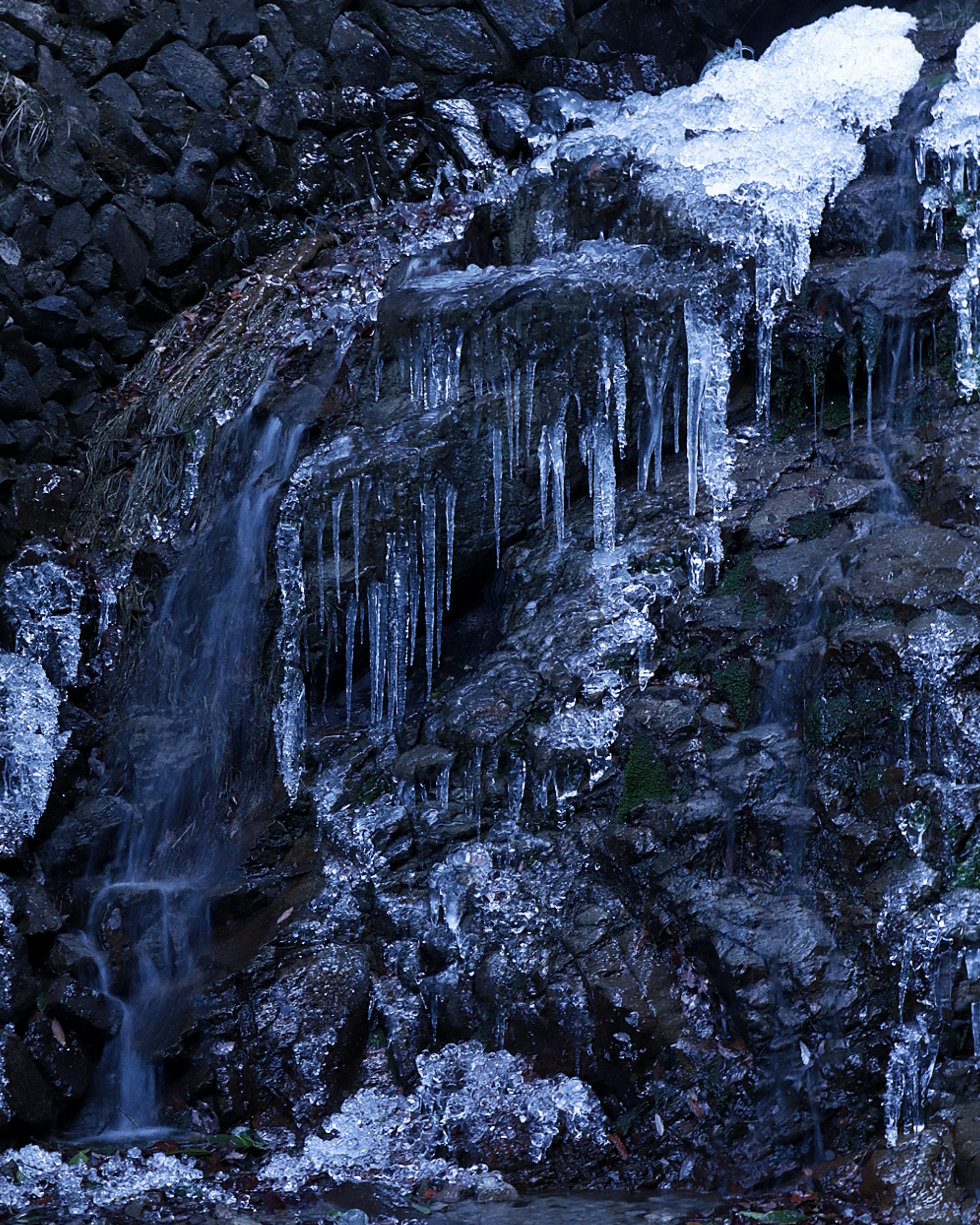 Cascata invernale con ghiaccioli e acqua che scorre