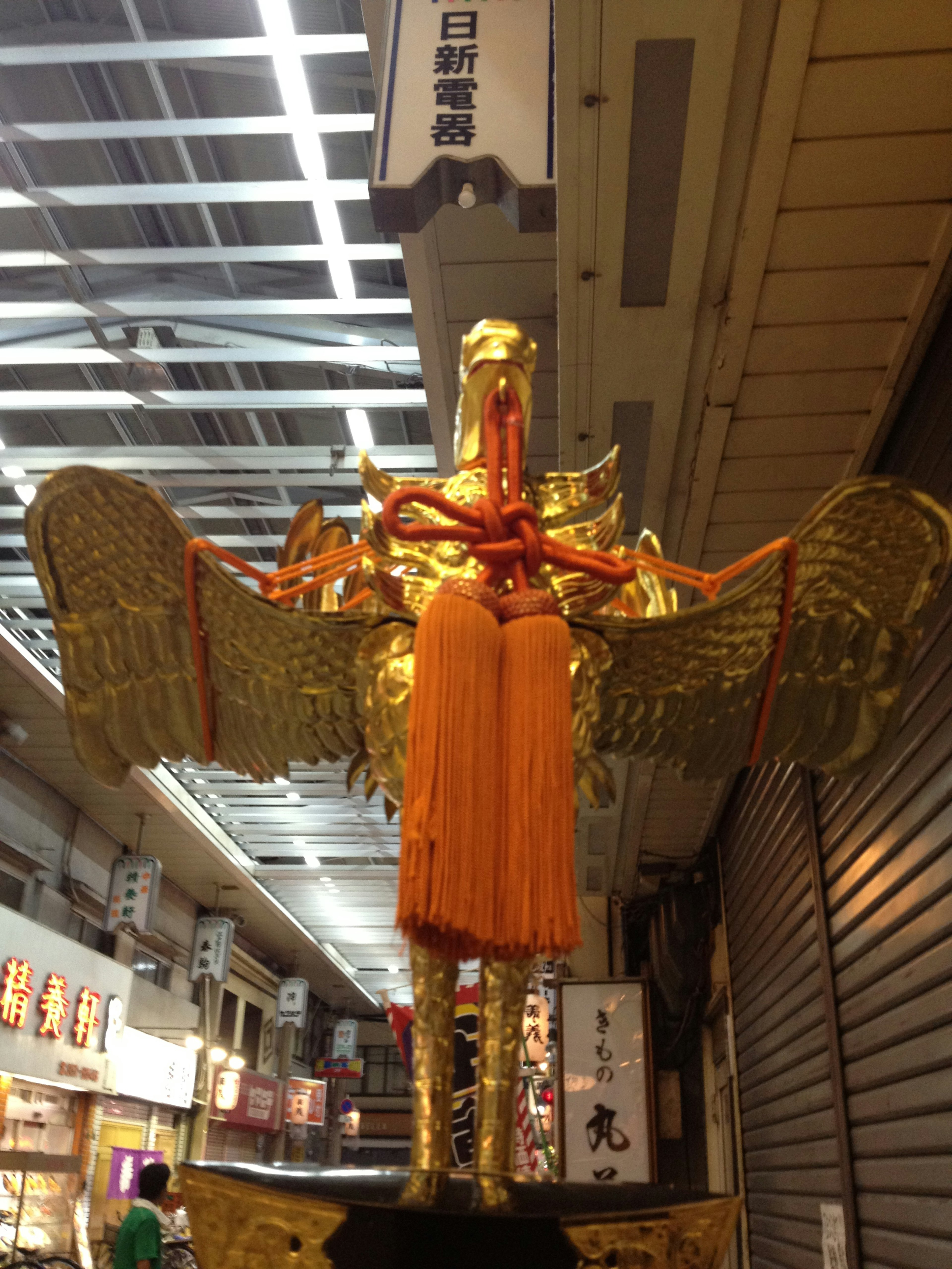 Statue d'oiseau dorée ornée de tissu orange dans une arcade commerçante