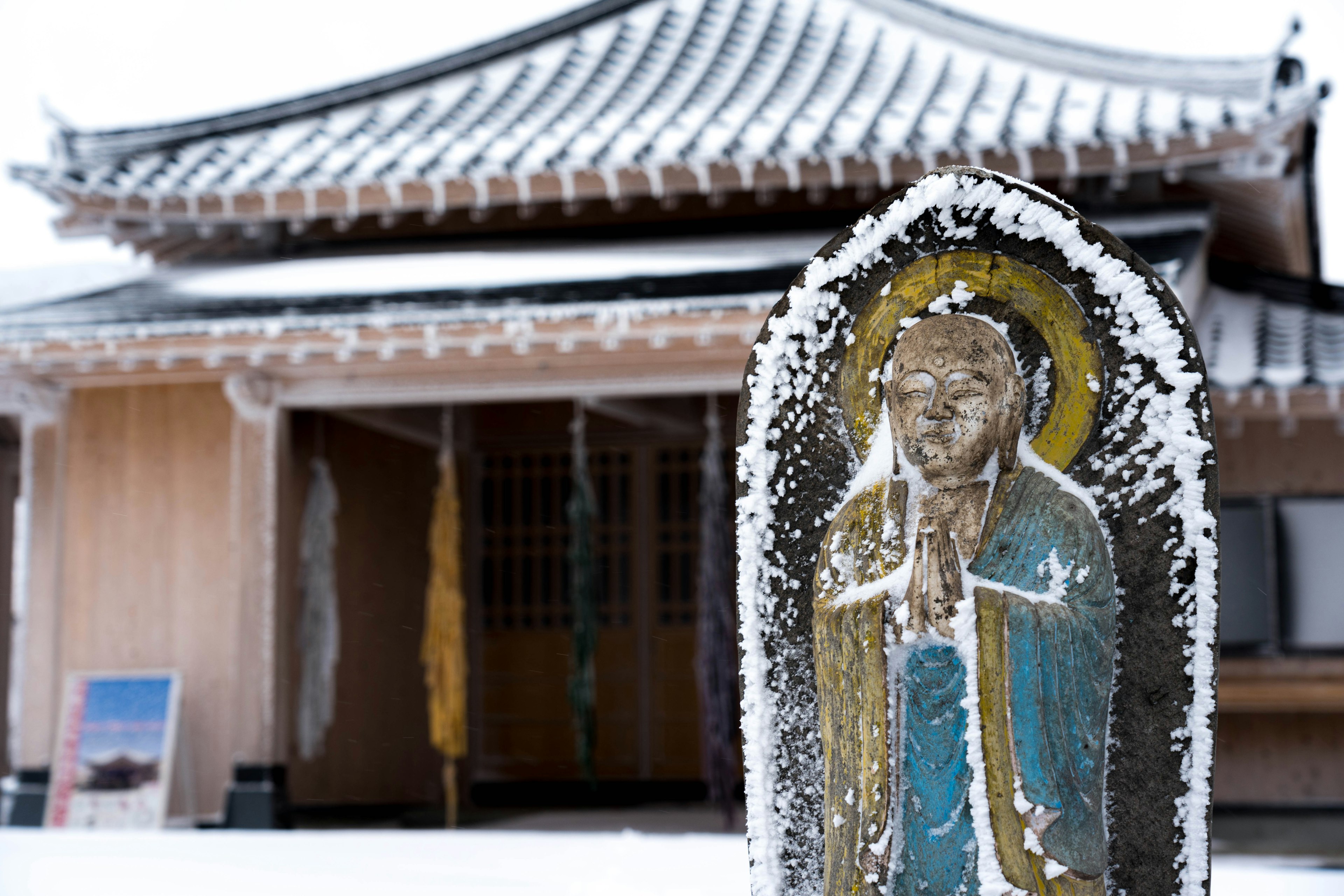 Estatua de Buda cubierta de nieve con un edificio tradicional al fondo