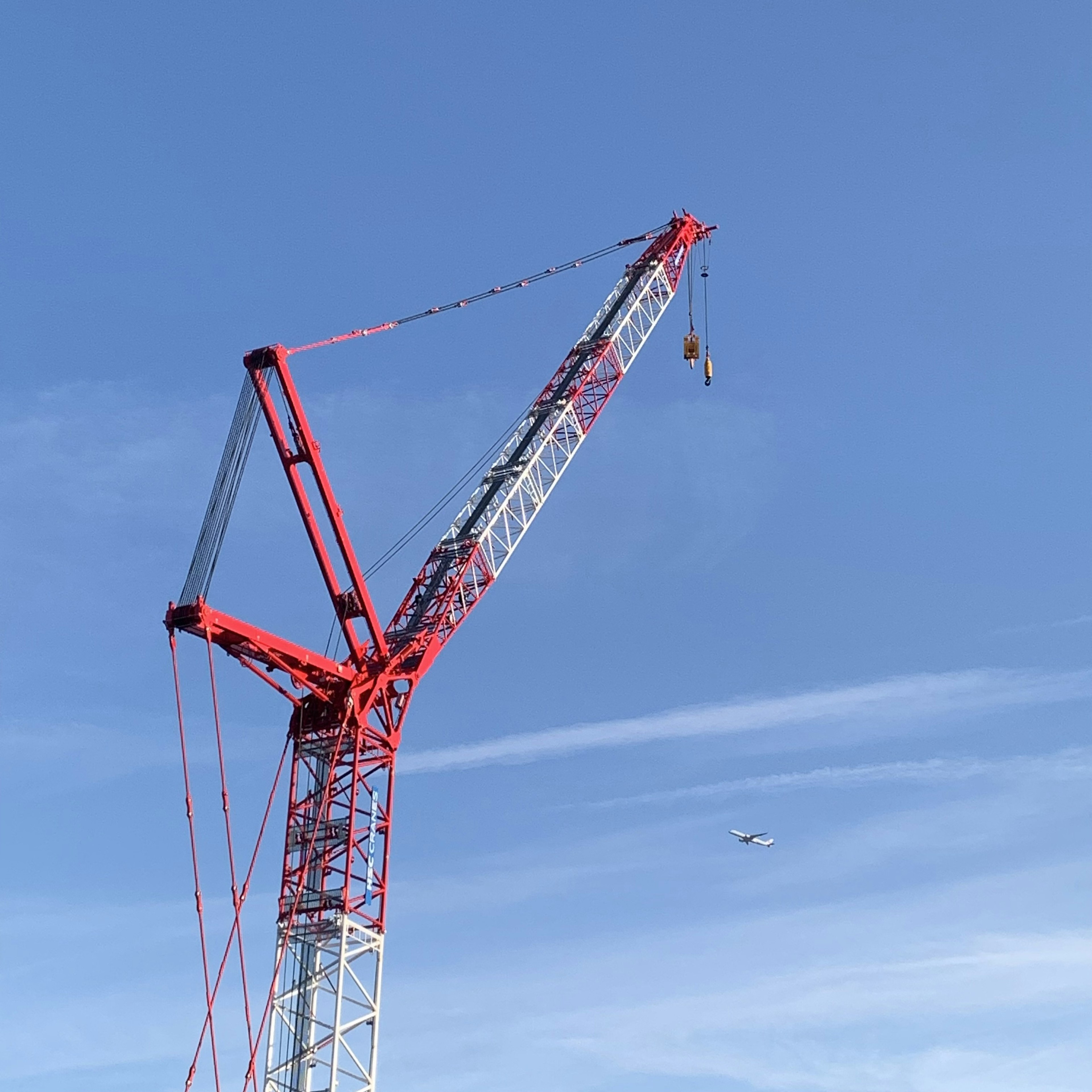 Red crane structure under blue sky with suspended load