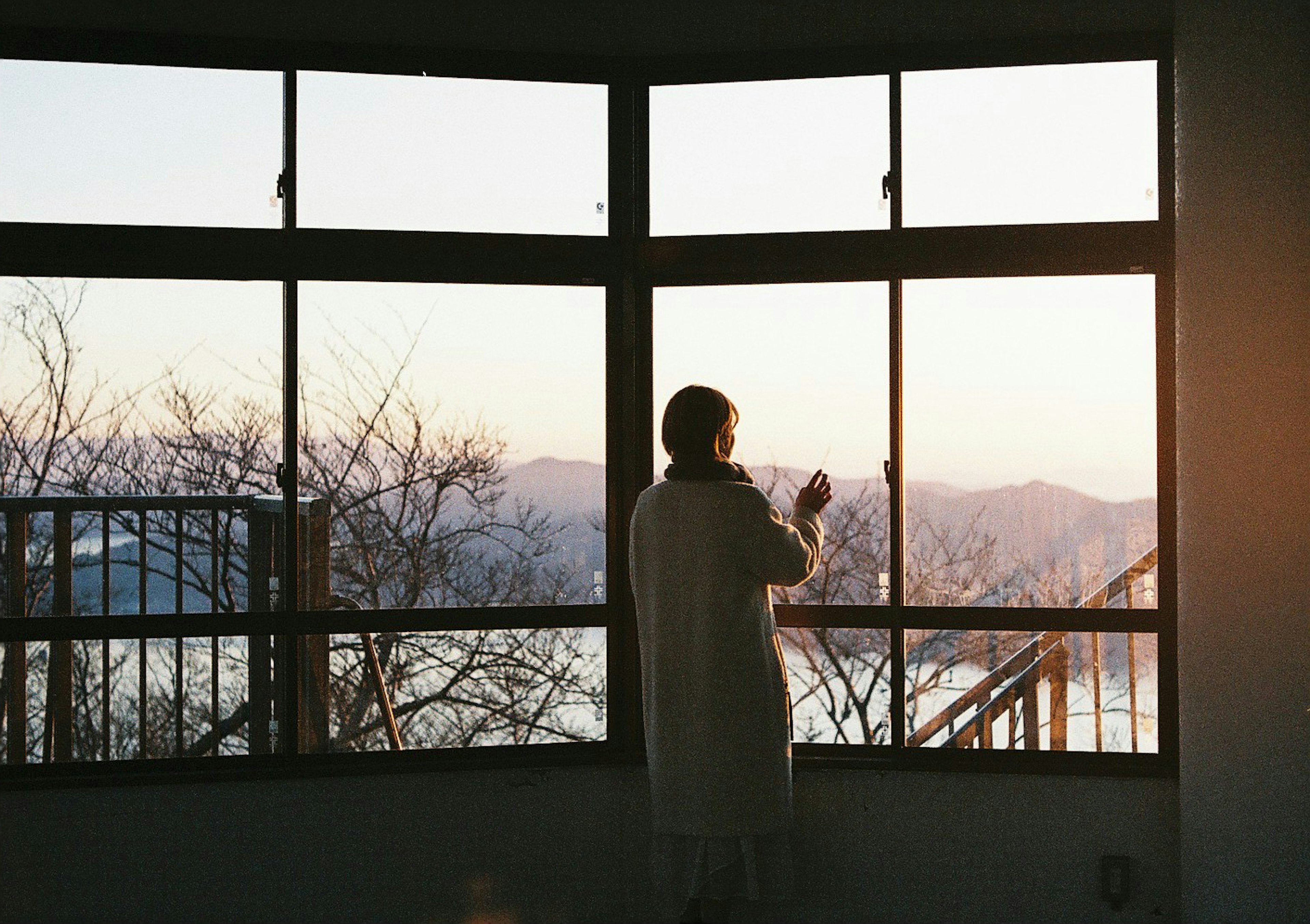 Person gazing out the window at sunset with mountains in view