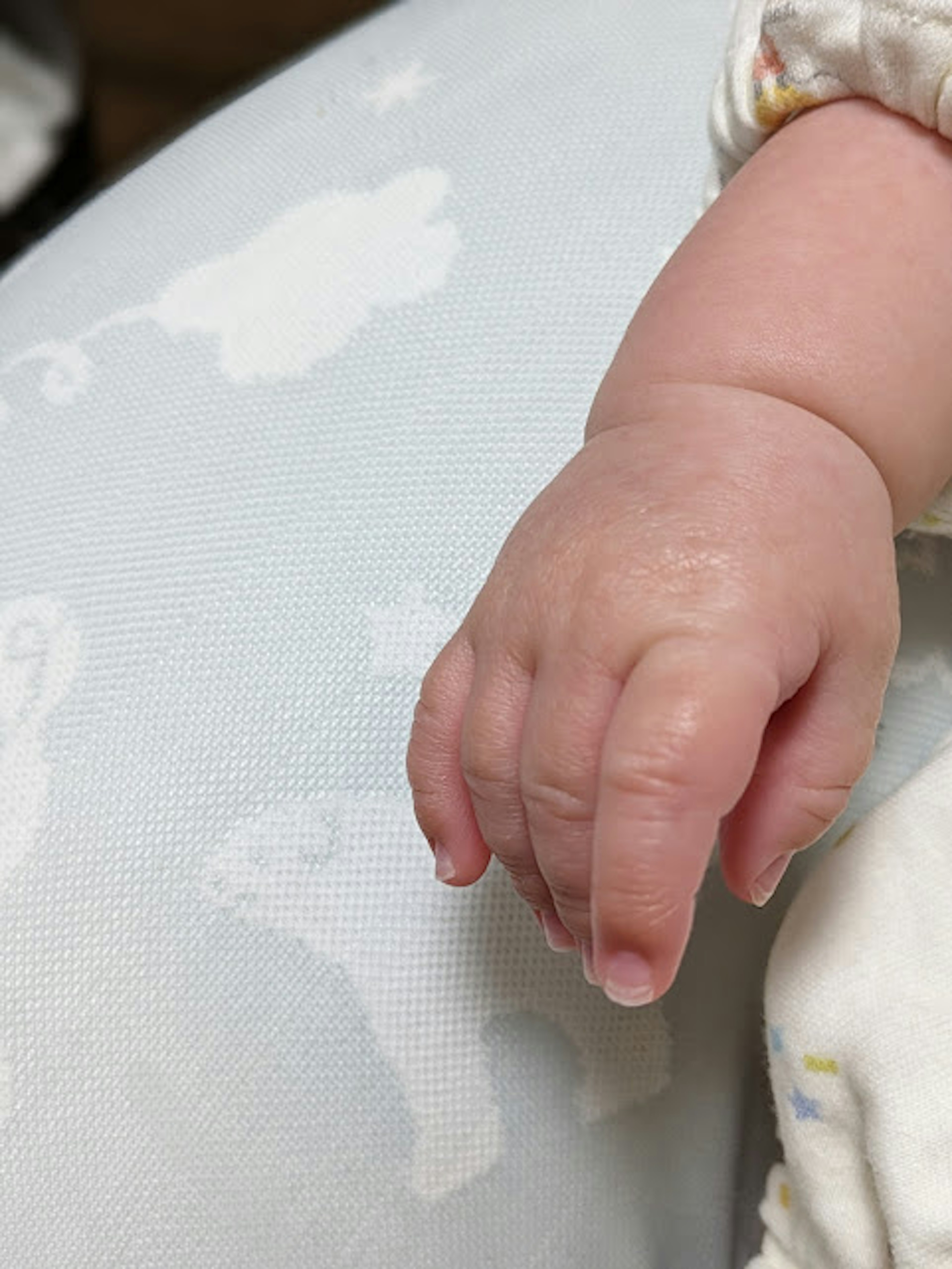 Eine Hand eines Babys, die auf einem weichen weißen Stoff ruht