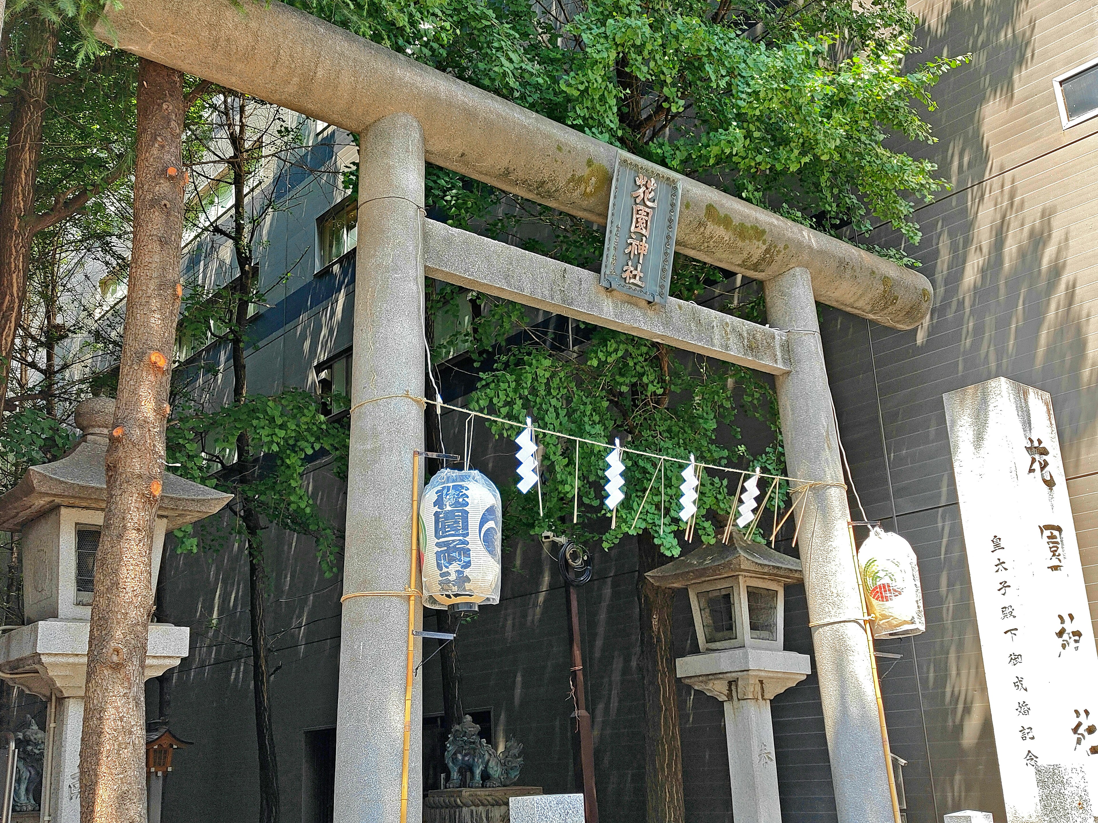 Eingang eines Schreins mit Torii und Laternen, umgeben von Grün