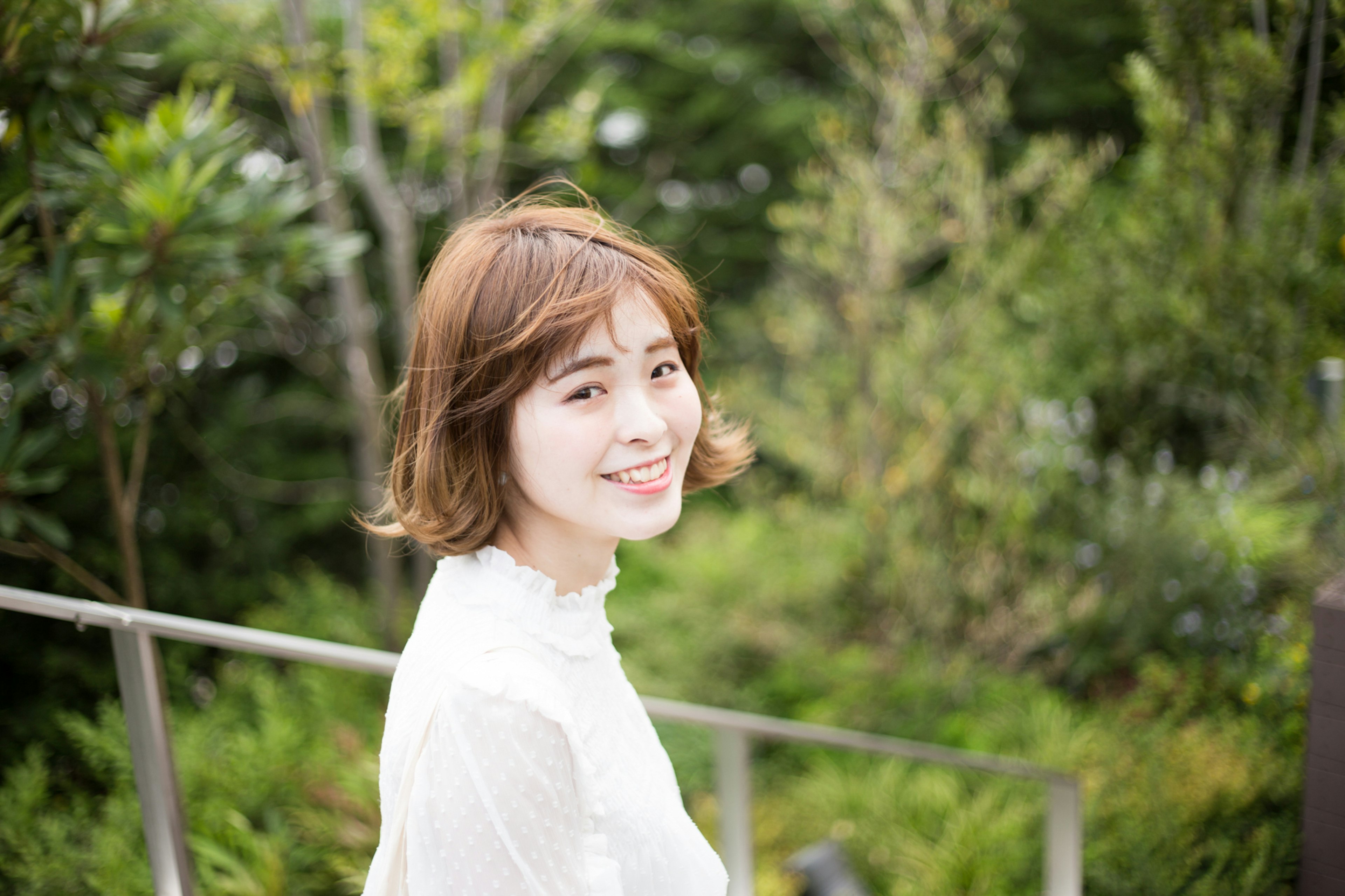 Smiling woman in a white top with a lush green background